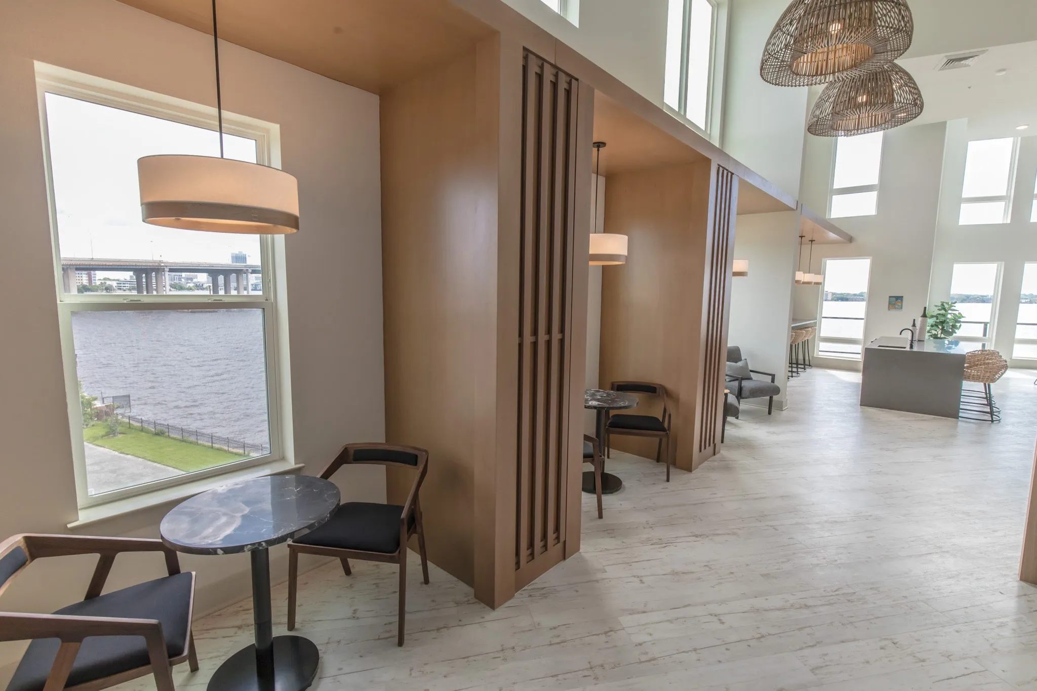 Multifamily amenity work booth with a marble cafe table and black chairs by a river view window, the island beyond