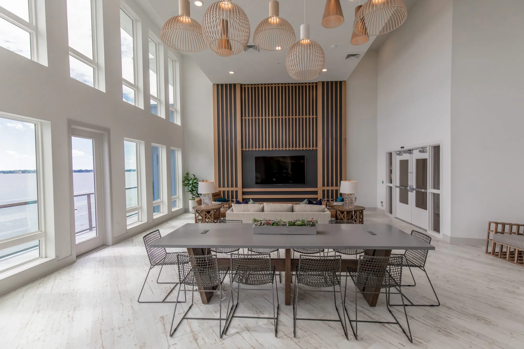 Multifamily amenity clubroom with a long table and wire chairs before the wood slat media wall and sofa