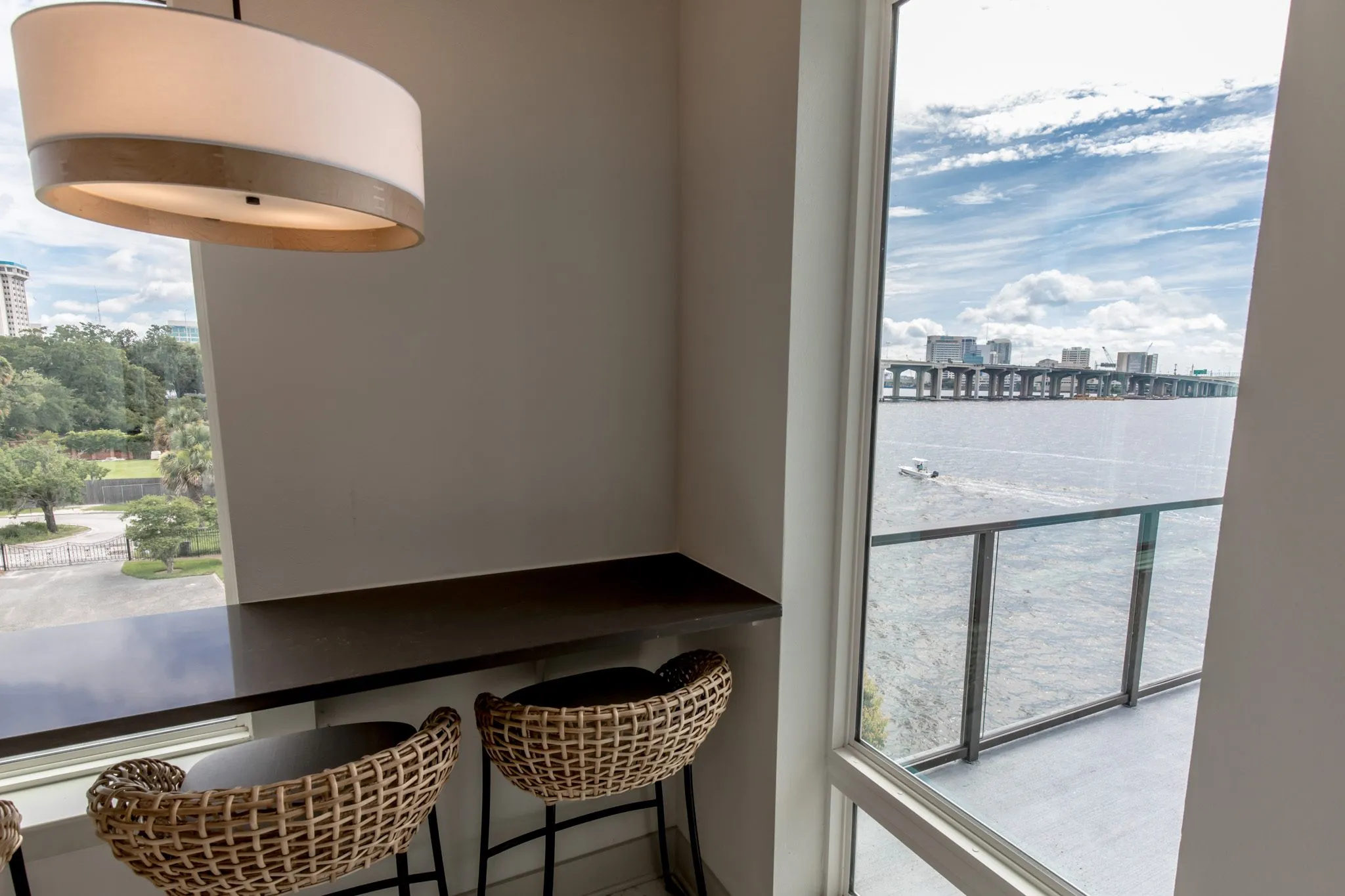Multifamily amenity window bar with two woven stools under a drum pendant, the river and bridge through the glass