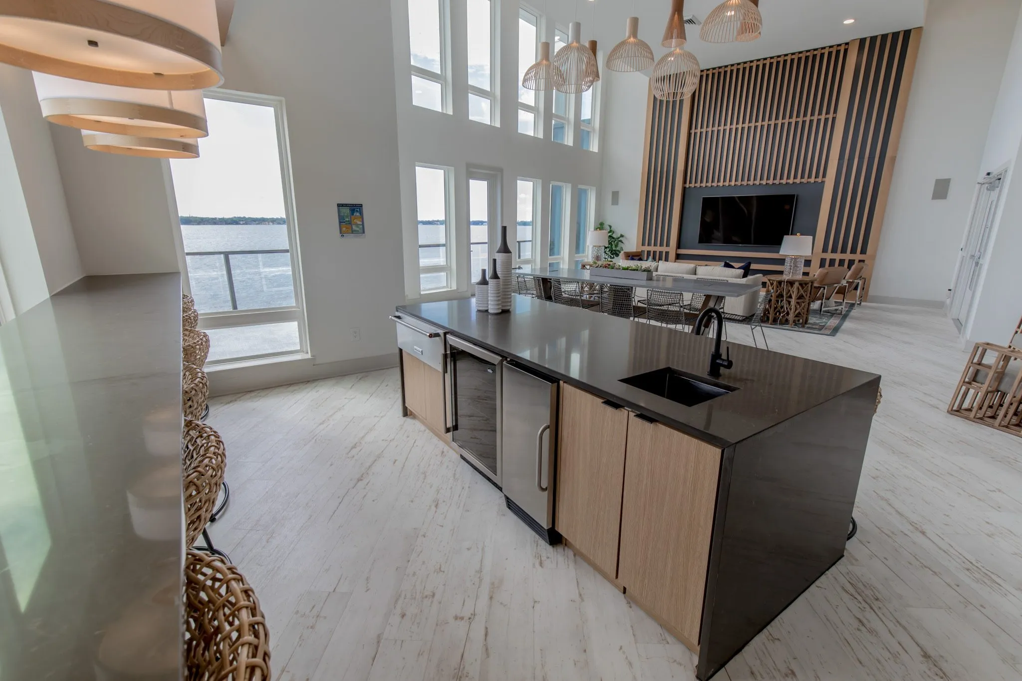 Multifamily kitchen island with a black counter, oak cabinets and wine fridge, the media wall and table beyond