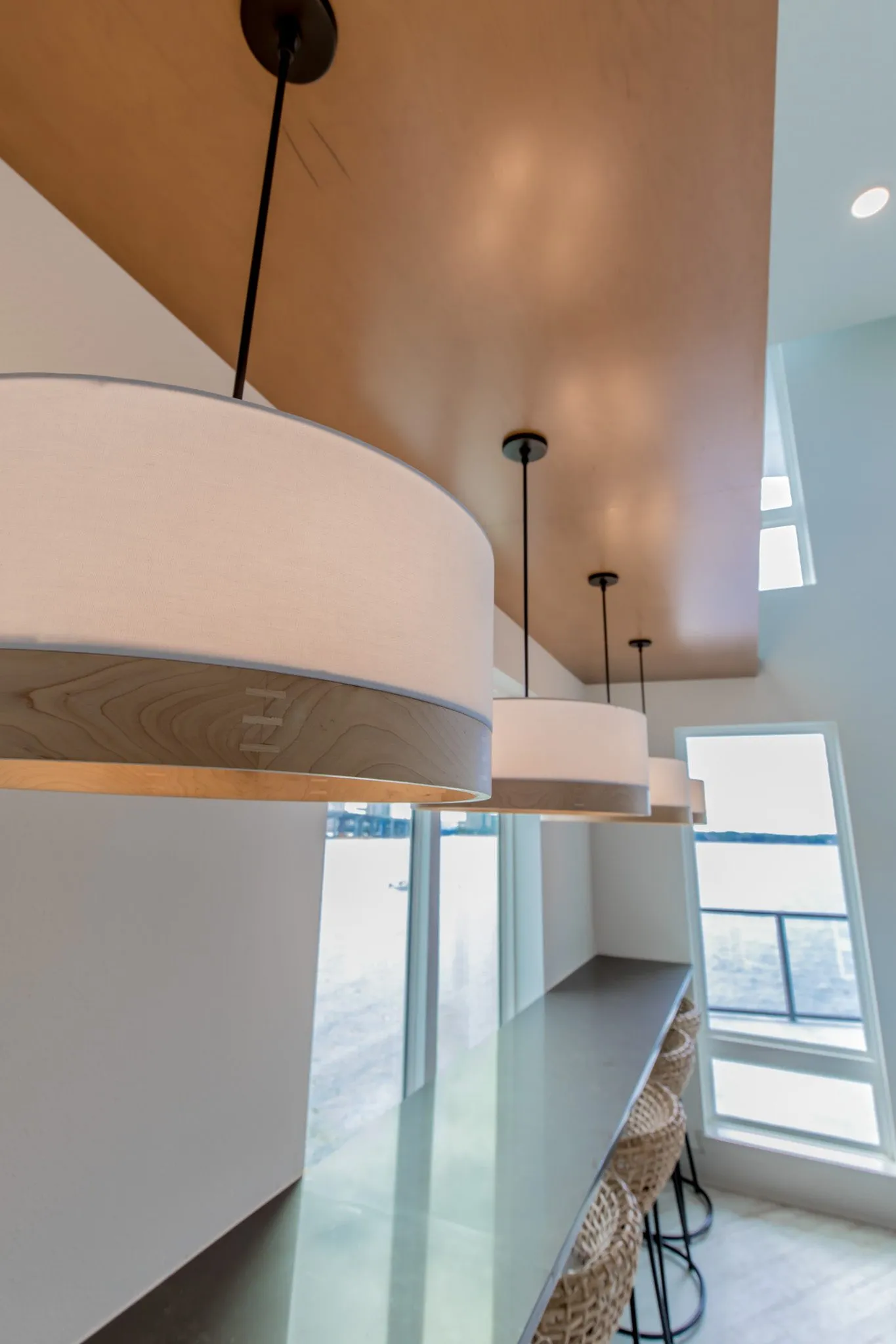 Multifamily interior detail: drum pendants over the window bar toward a tall window, a wood soffit above