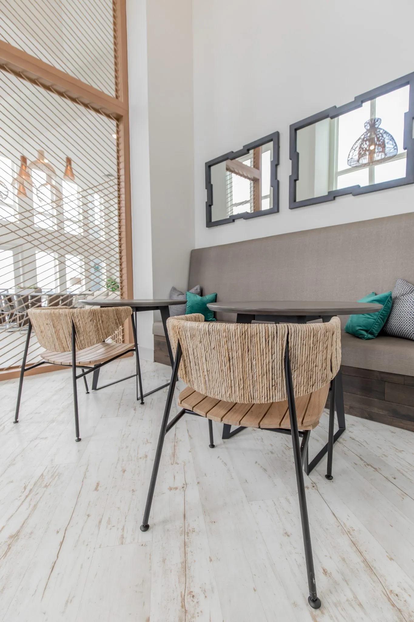 Multifamily amenity clubroom with woven chairs at cafe tables before the grey banquette and black framed mirrors