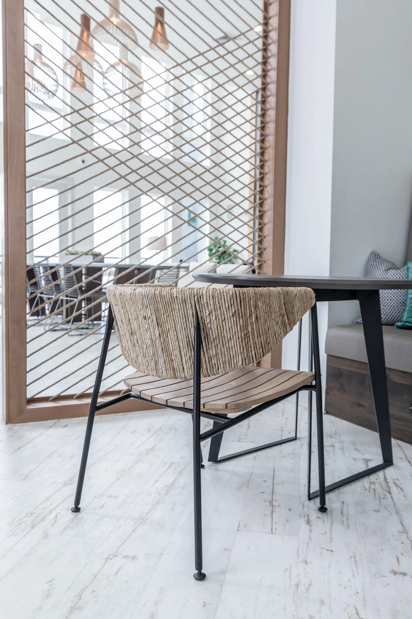 Multifamily interior detail: woven back chair with a slatted wood seat at a table beside the rope screen
