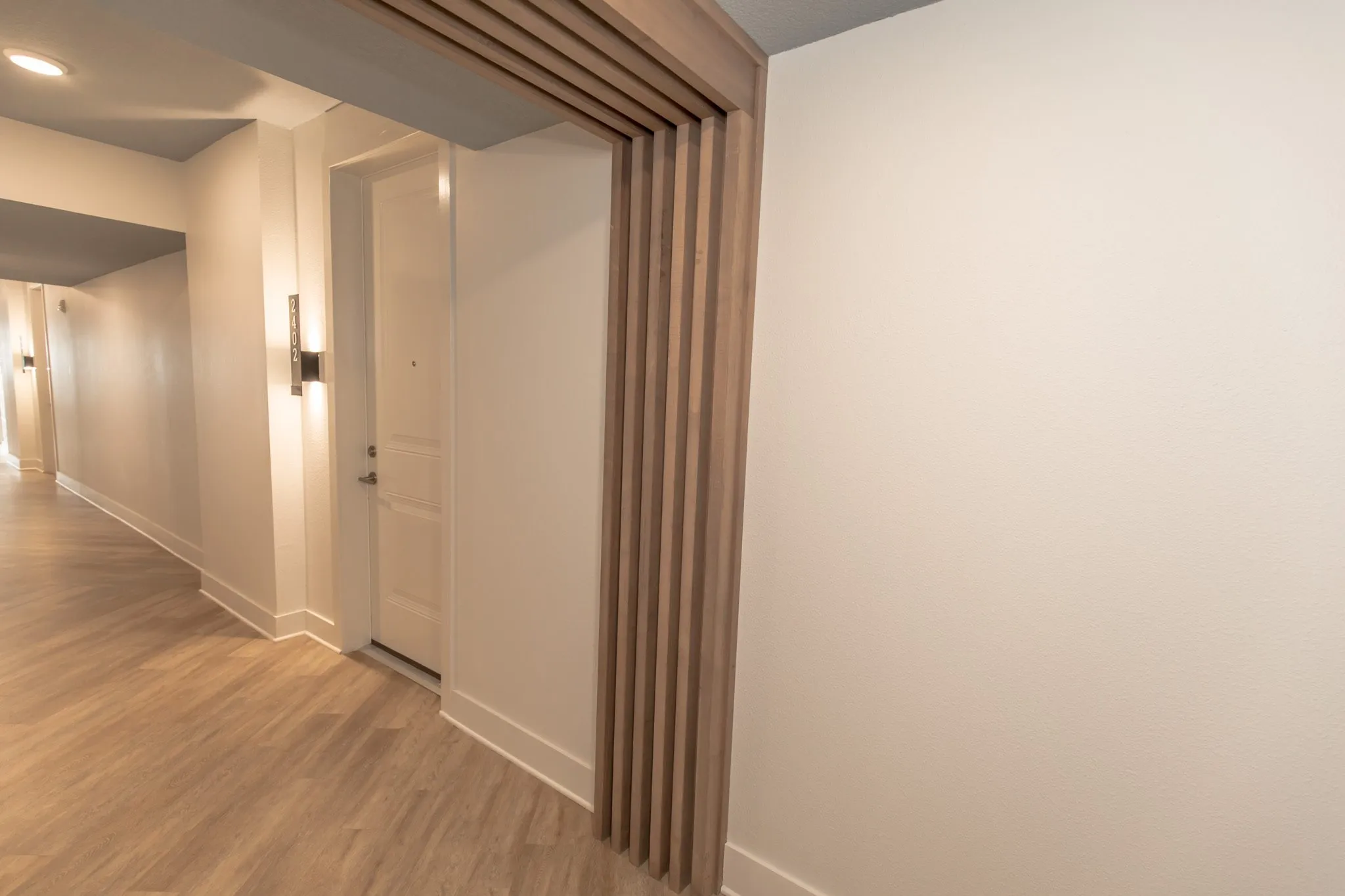 Multifamily residential corridor with a wood slat portal framing an apartment door and wall sconce