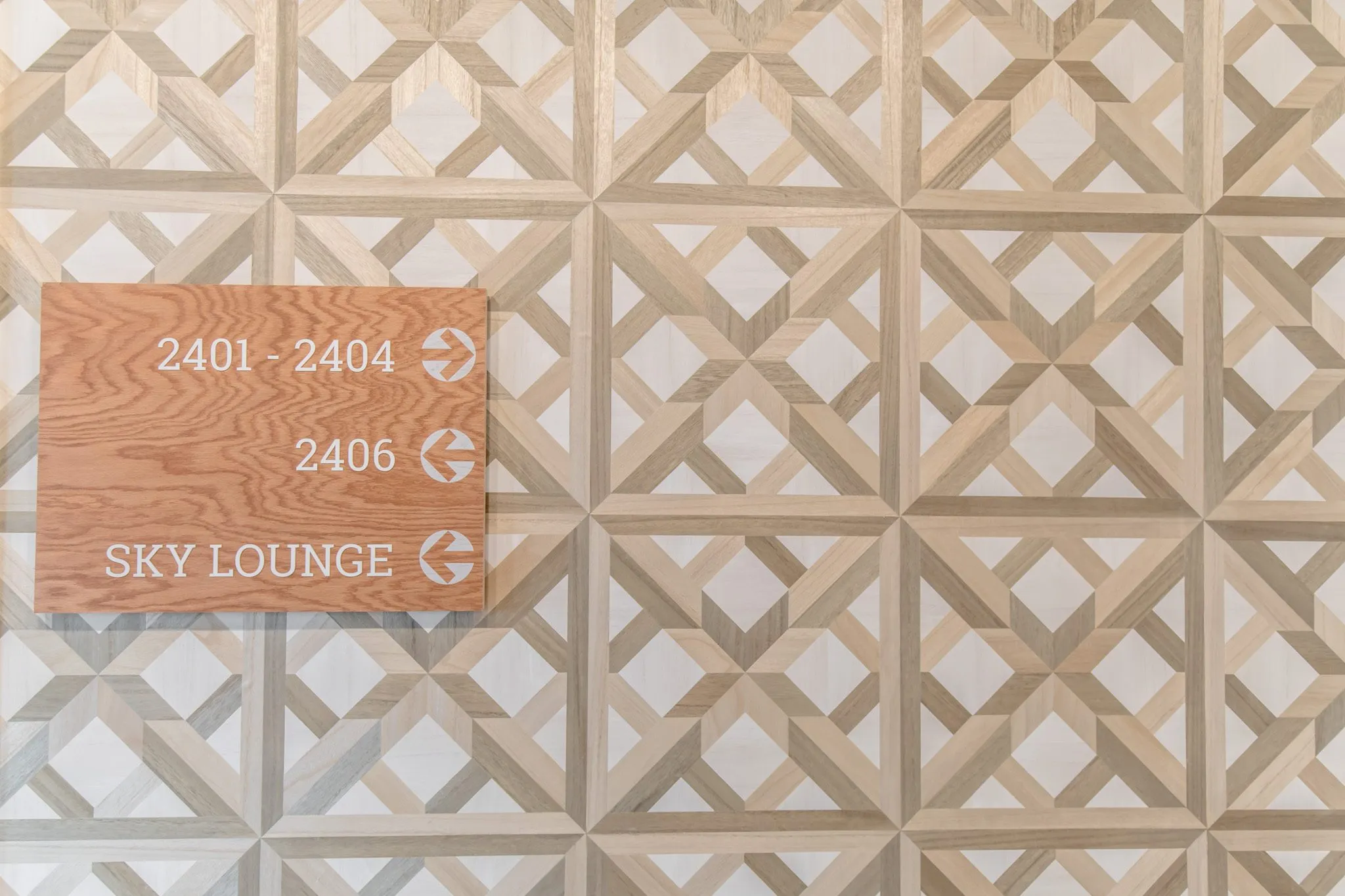 Multifamily interior detail: wood wayfinding sign for apartments and the sky lounge on parquet pattern wallcovering