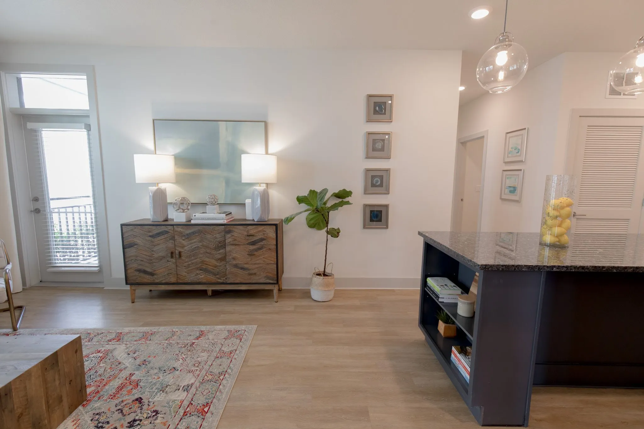 Multifamily model apartment living area with a herringbone wood sideboard, lamps and fig tree, a navy kitchen island