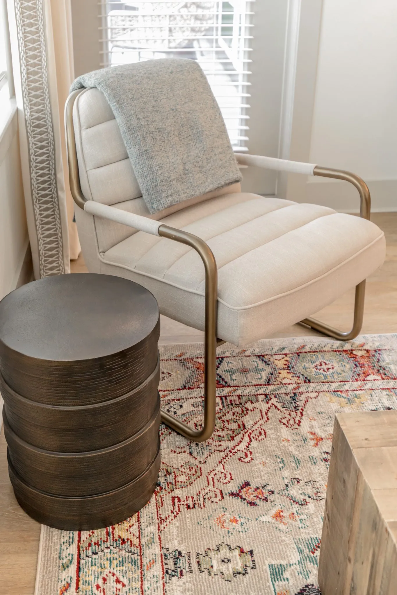 Multifamily interior detail: cream channel tufted armchair with brass frame and a throw beside a metal drum table