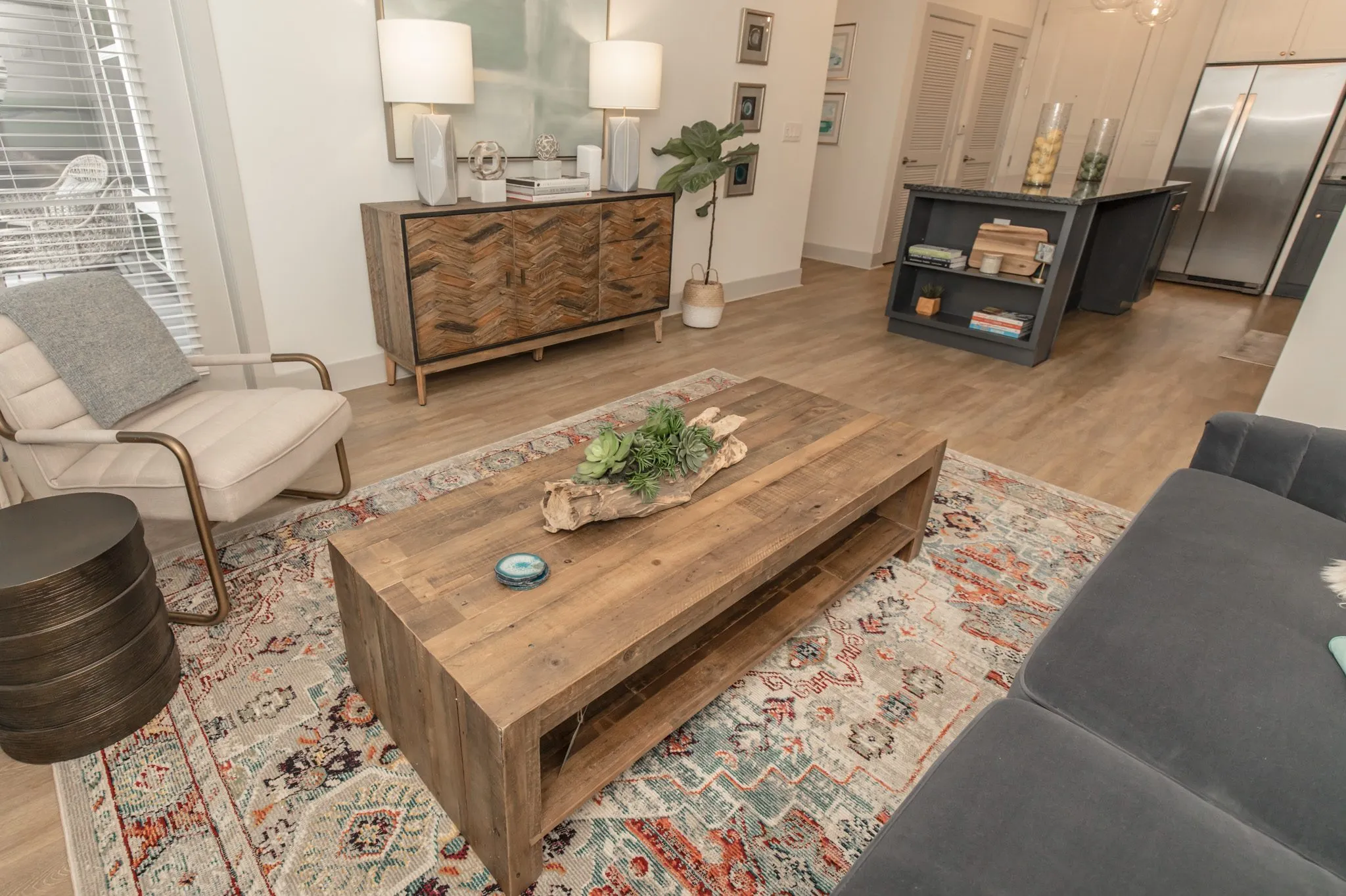 Multifamily apartment living room from above, a reclaimed wood coffee table on a patterned rug, sideboard and kitchen island