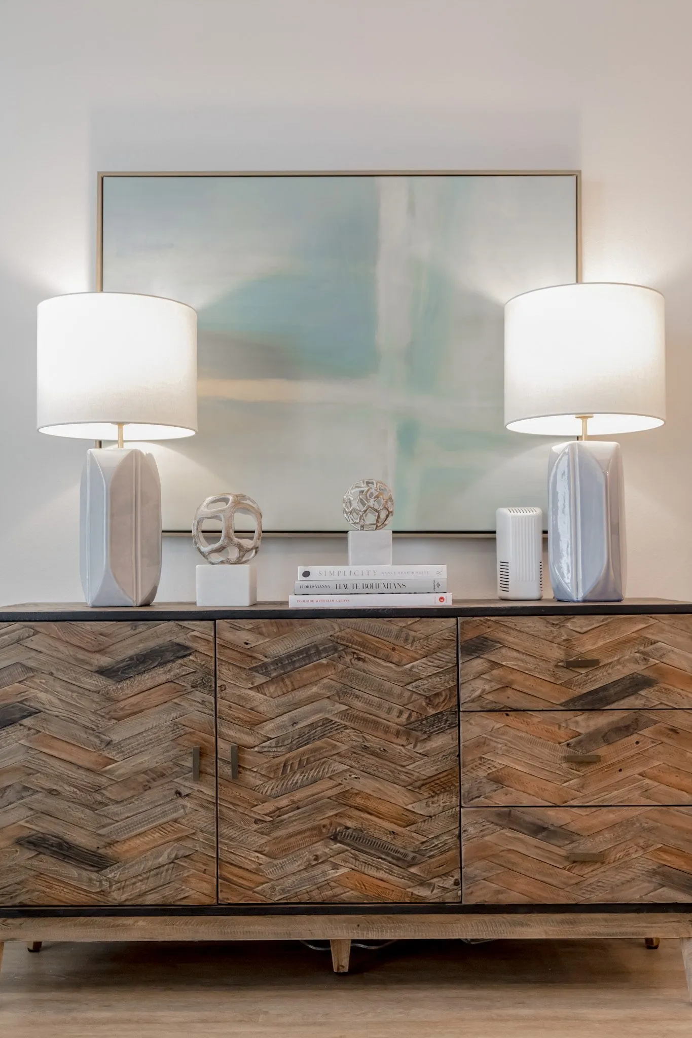 Multifamily interior detail: herringbone wood sideboard with white lamps and sculptures below an abstract painting