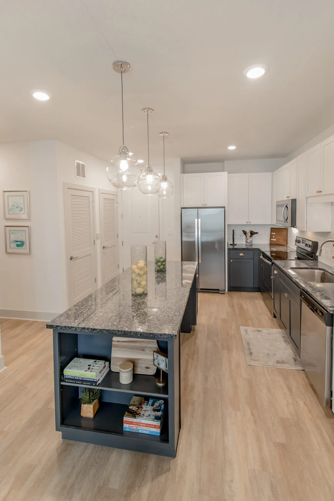 Multifamily model apartment kitchen with a navy island under glass globe pendants, grey lower and white upper cabinets