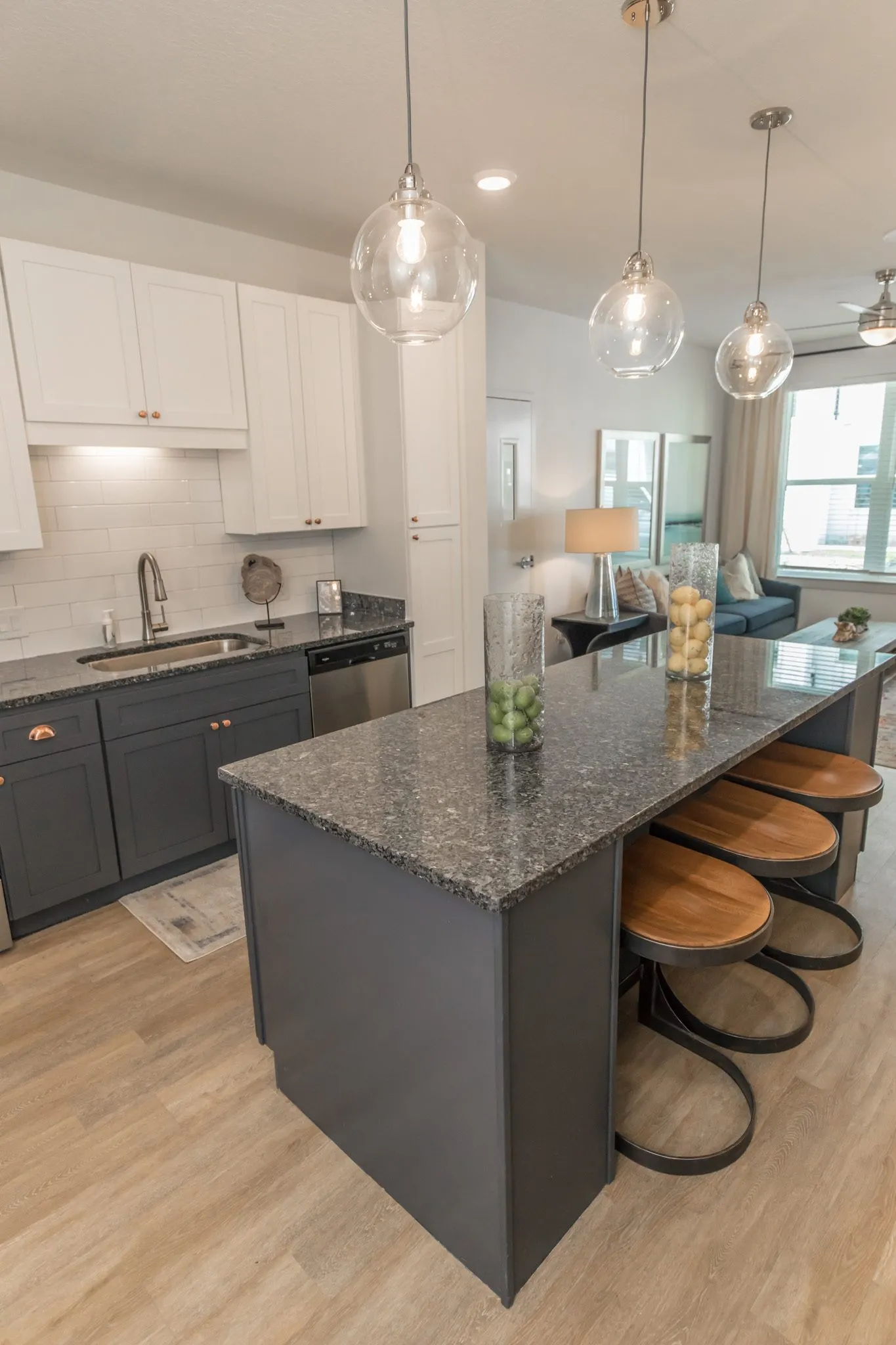 Multifamily kitchen island in granite with wood seat stools under glass pendants, the living room beyond