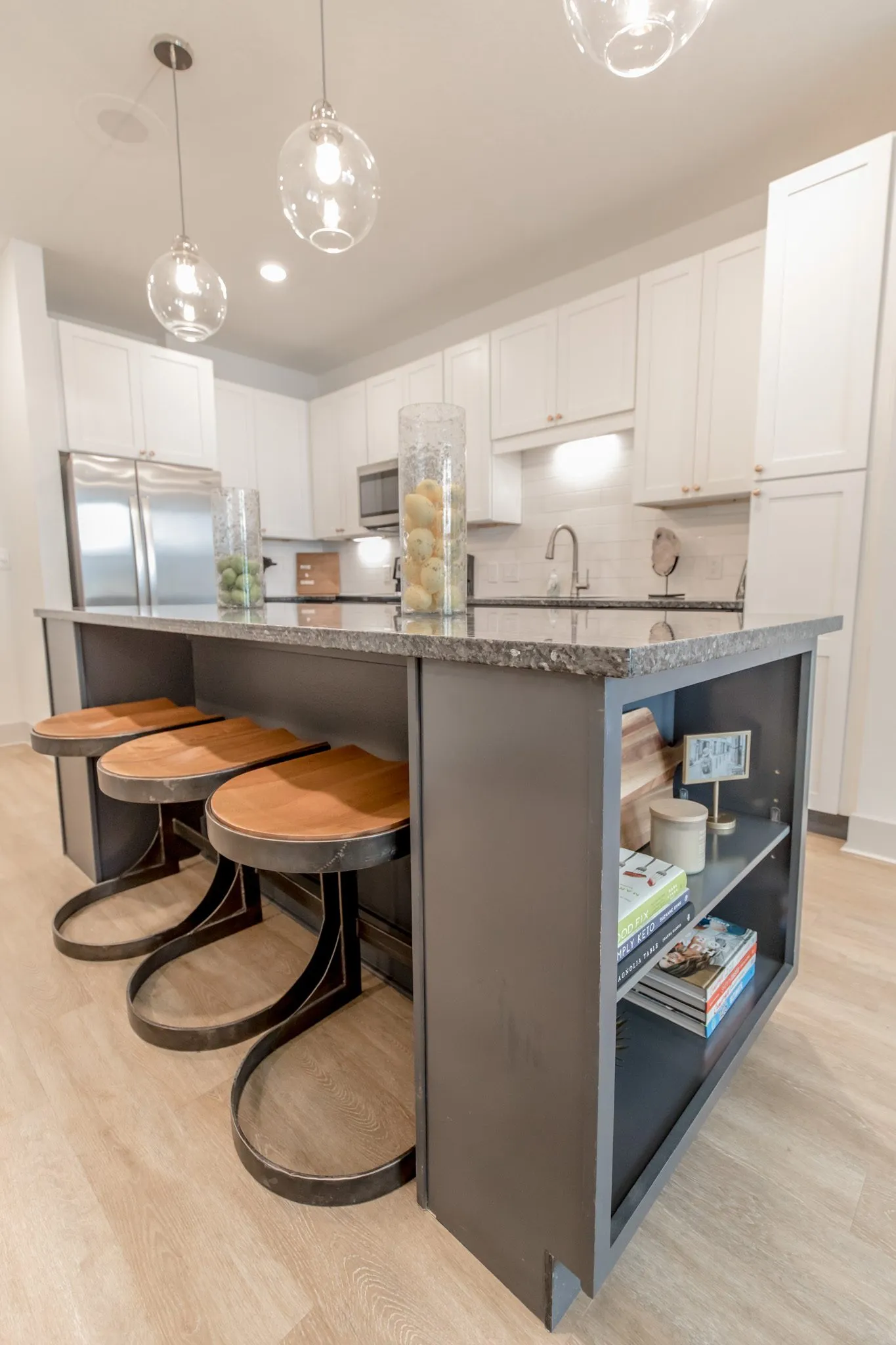 Multifamily kitchen: low view of the island's open shelf end and wood stools, white cabinets and refrigerator behind