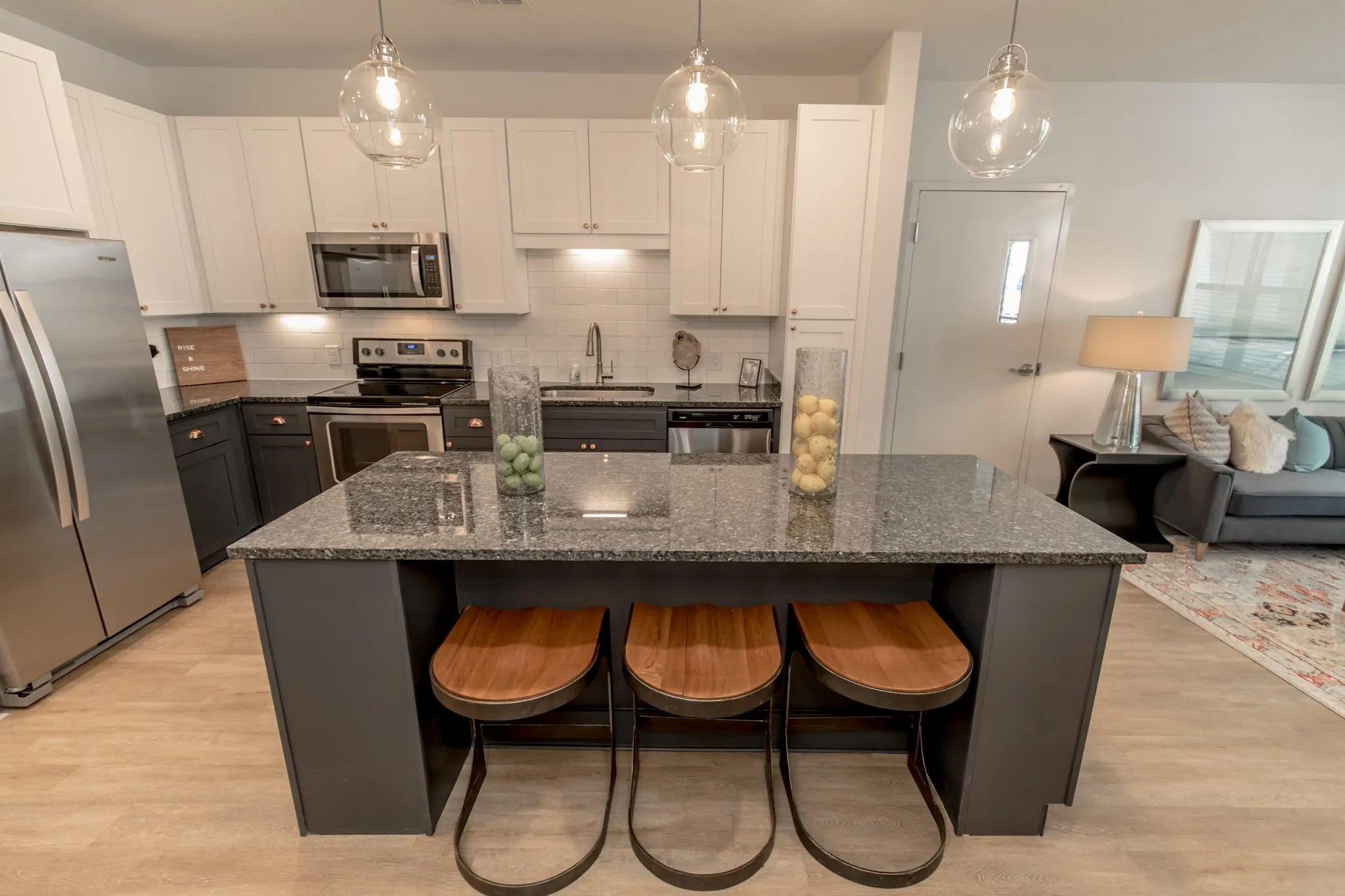 Multifamily kitchen with three wood seat stools at the granite island, range and microwave behind