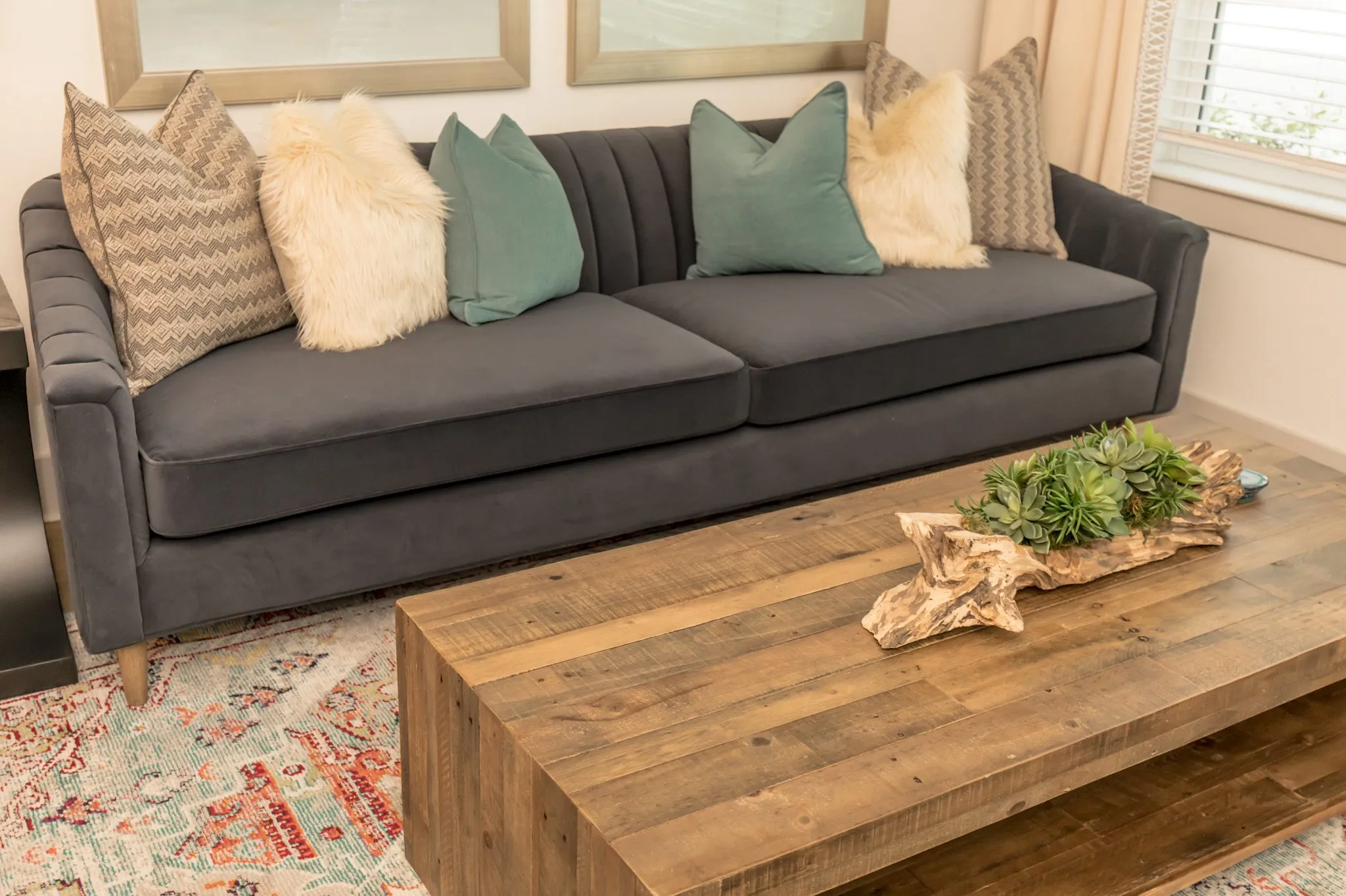 Multifamily interior detail: charcoal velvet sofa with green and sheepskin pillows behind a reclaimed wood coffee table