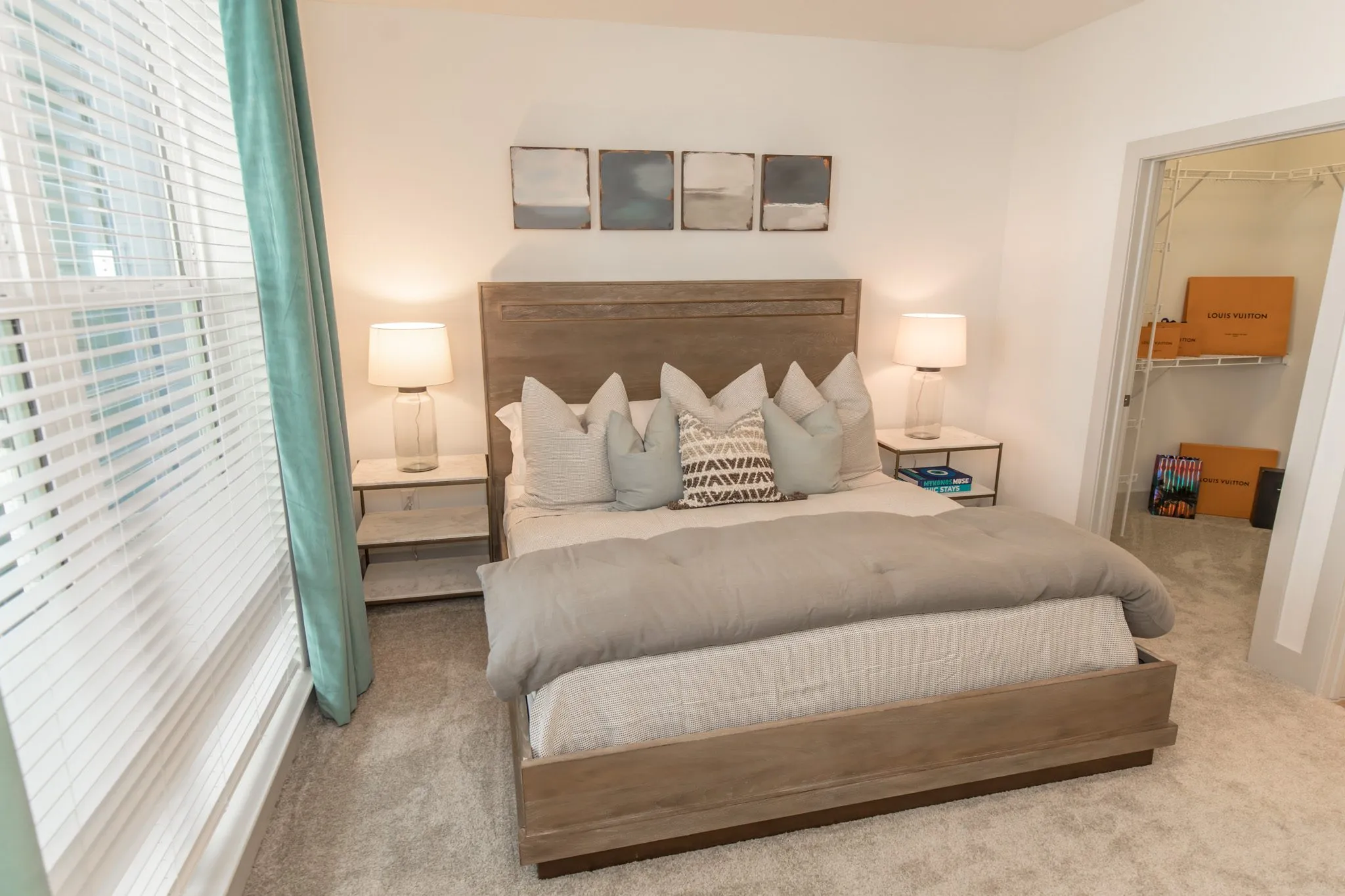 Multifamily model apartment bedroom with a wood headboard, grey bedding and teal curtains, the walk-in closet beyond