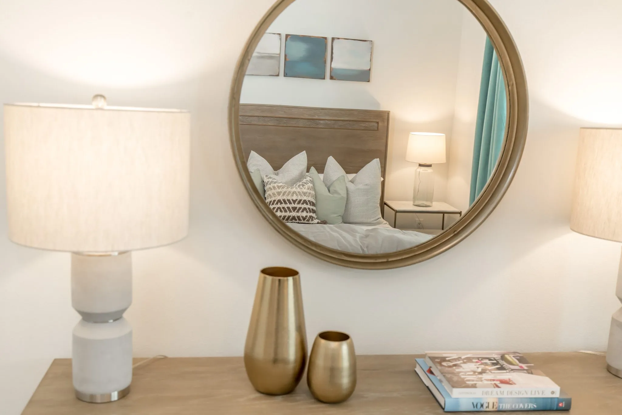 Multifamily apartment bedroom detail: brass vases and books on a dresser, the round mirror reflecting the bed and prints