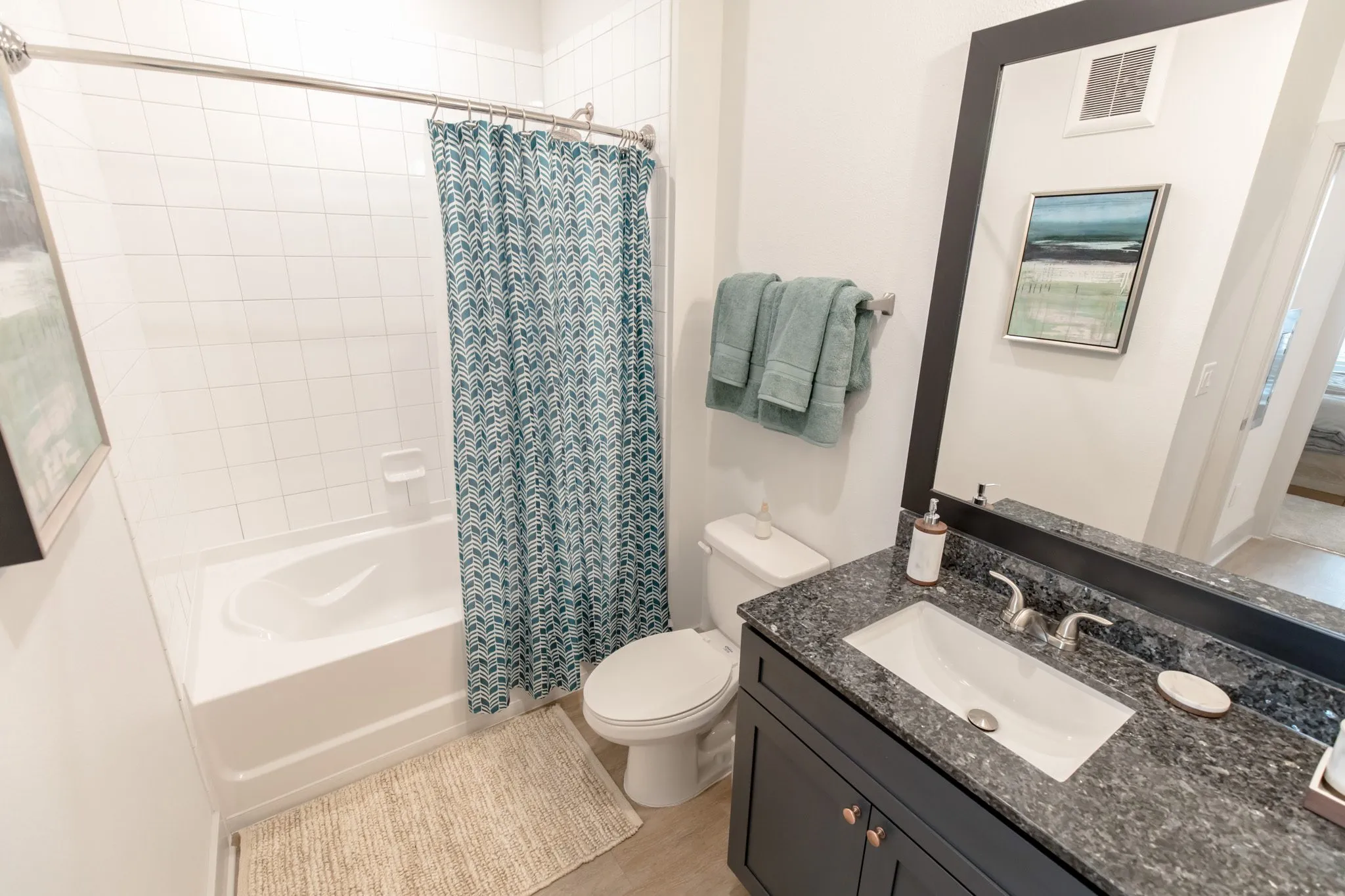 Multifamily model apartment bathroom with a granite vanity, teal patterned shower curtain and white subway tile surround