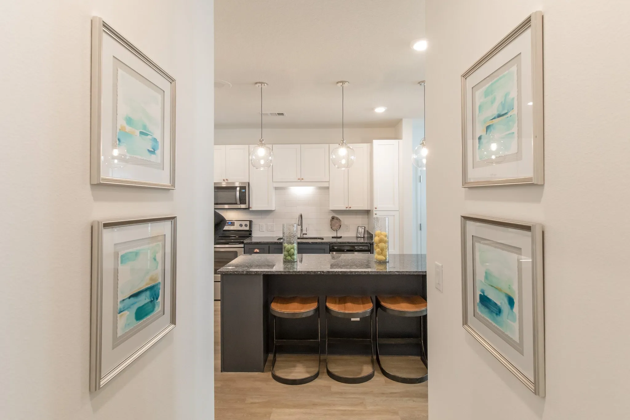 Multifamily hallway between framed watercolour prints looking to the kitchen island and its stools