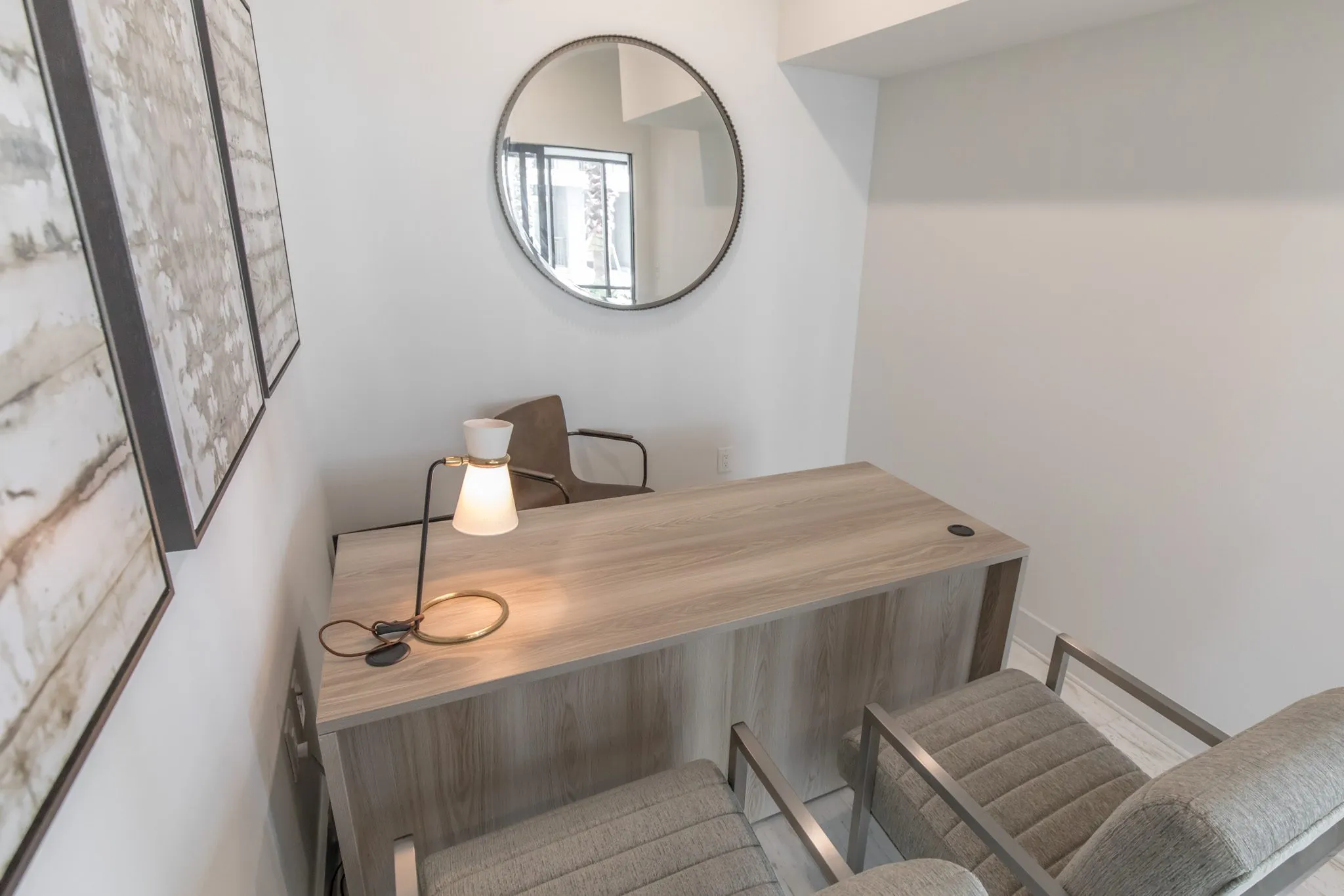 Multifamily amenity office desk with a white lamp seen from above, a round mirror on the wall and chairs in front