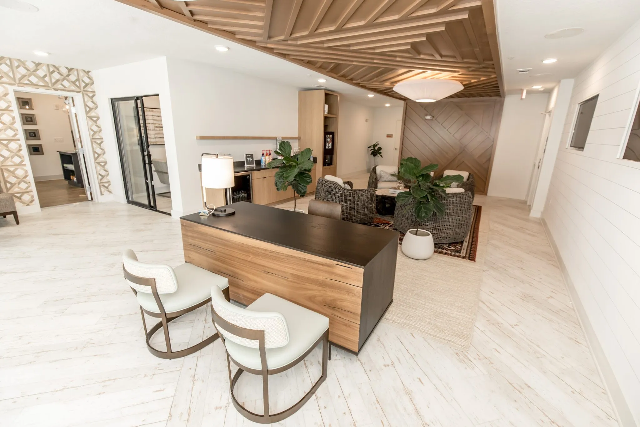Multifamily amenity leasing desk with two sage chairs, woven lounge chairs on a rug and a wood slat ceiling feature above