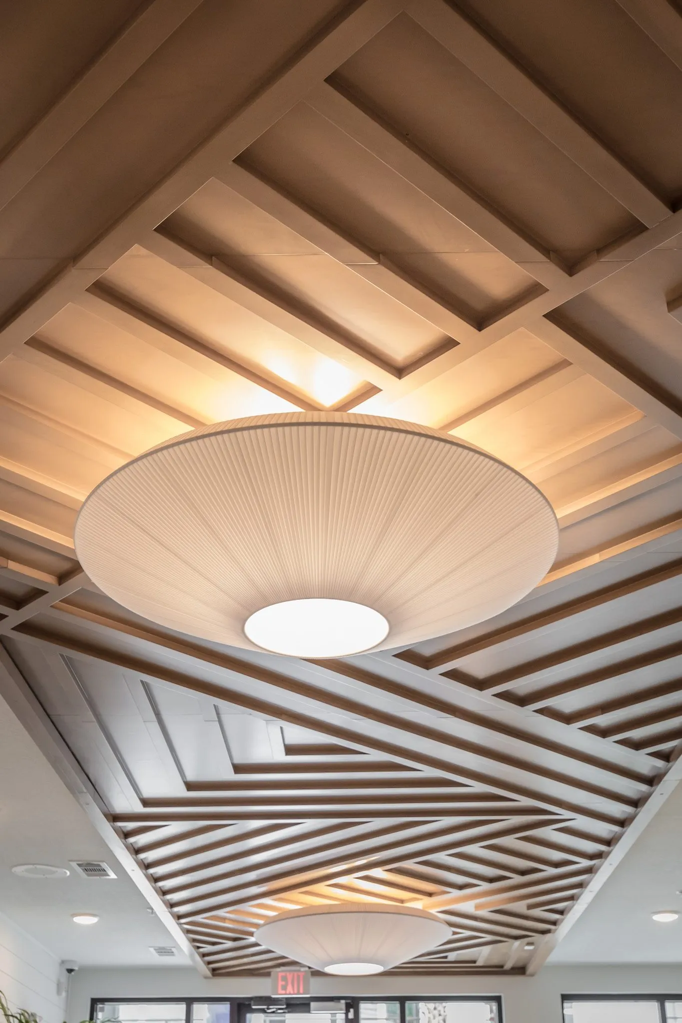 Multifamily interior detail: looking up at pleated fabric pendants hung from a diagonal wood slat ceiling feature