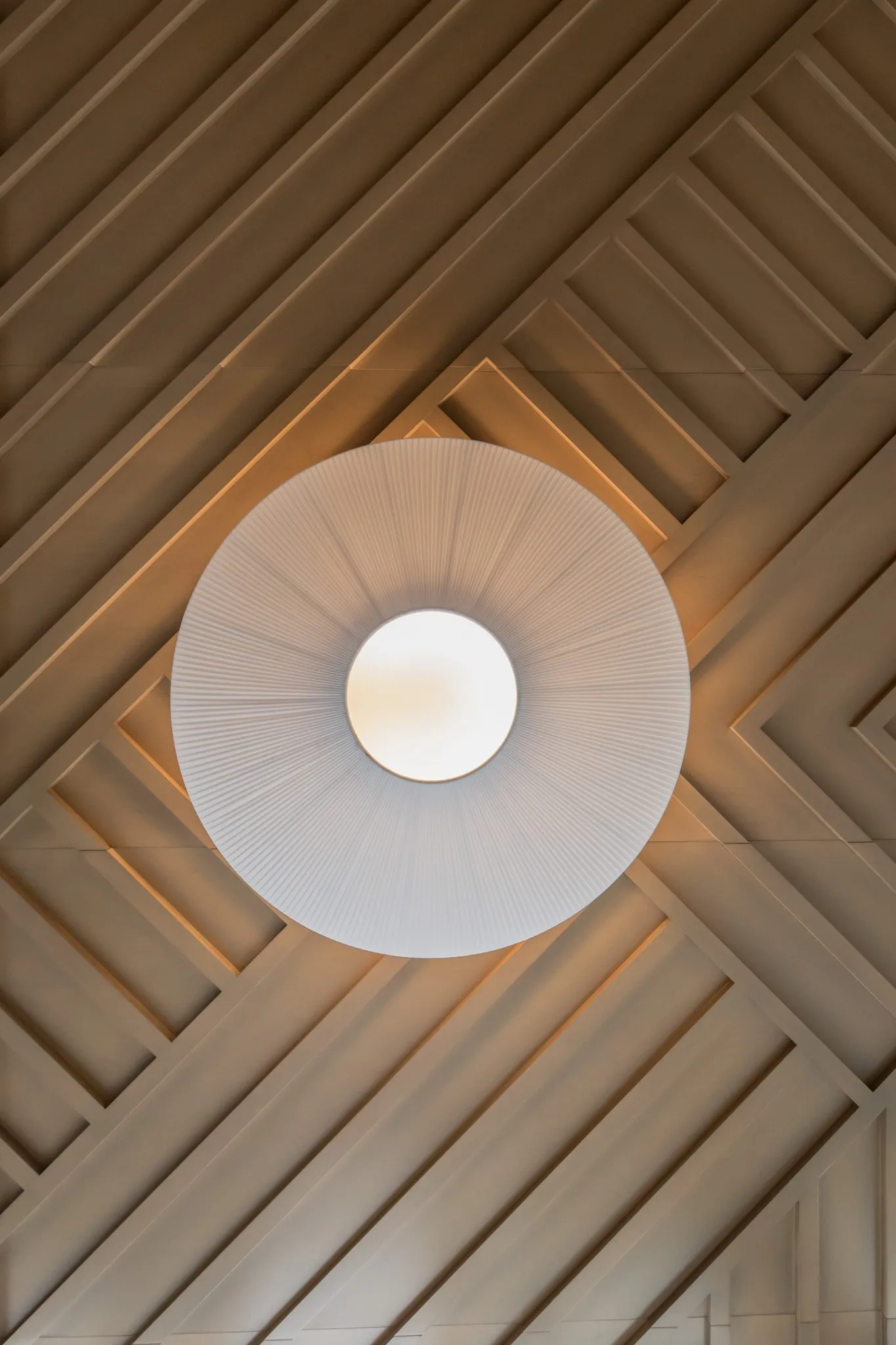 Multifamily interior detail: looking straight up at a pleated pendant against the diagonal wood slat ceiling