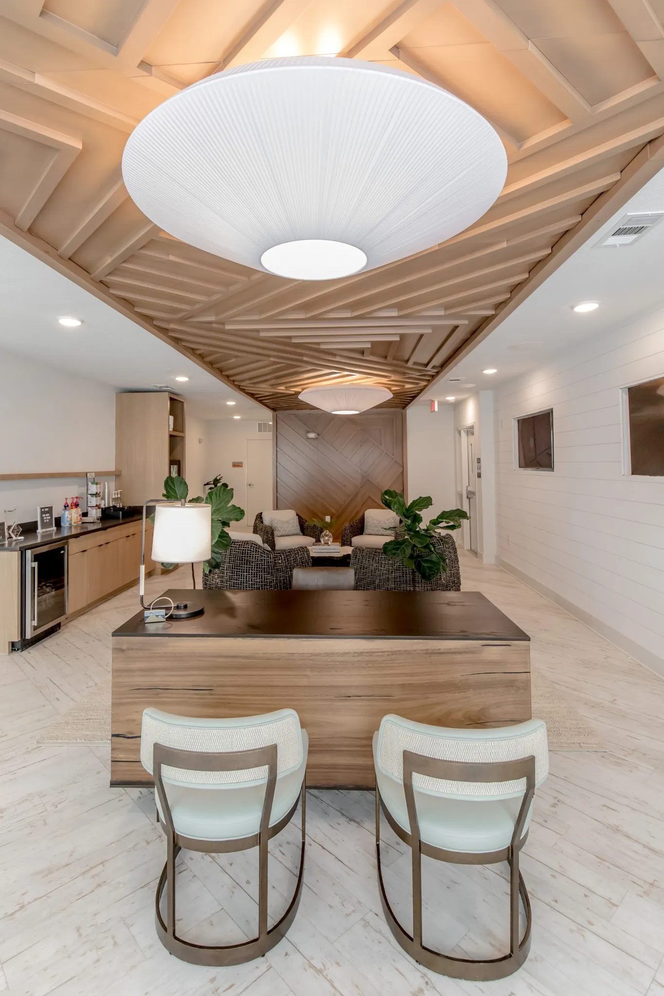 Multifamily amenity leasing desk with two sage chairs under pleated pendants and the slat ceiling
