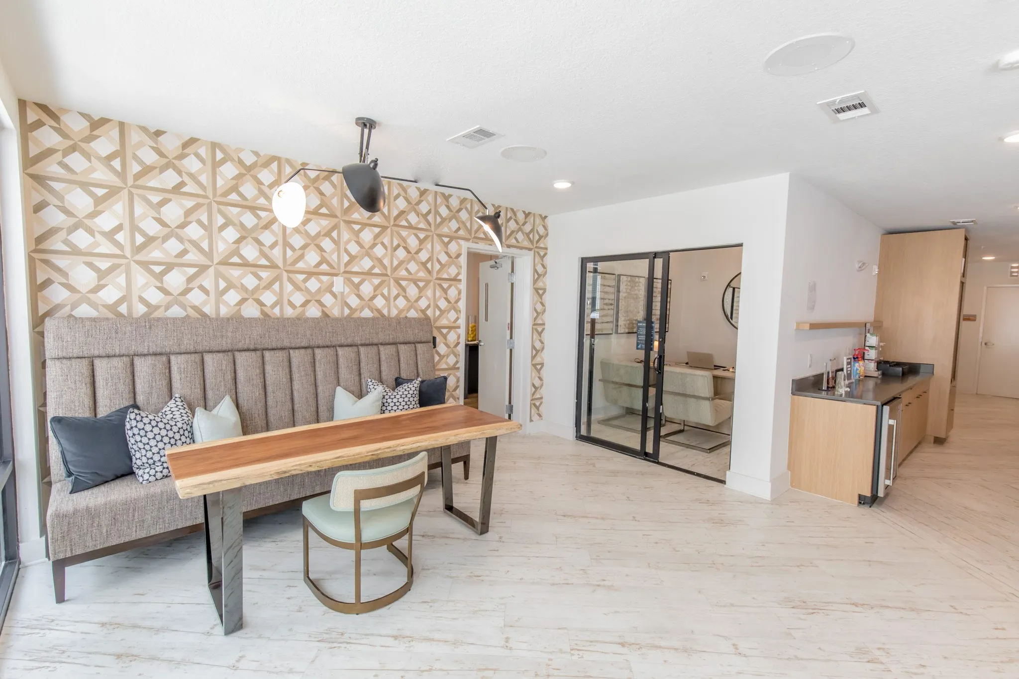 Multifamily amenity leasing area with a banquette, live edge table and sage chair, a glass-walled office and kitchenette