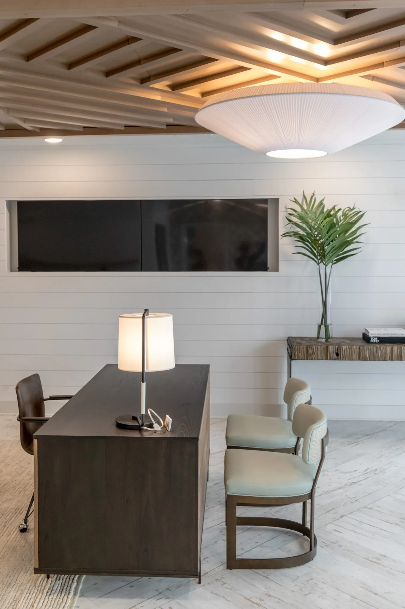 Multifamily interior detail: dark wood desk with a white lamp and two sage chairs below a wall screen on shiplap