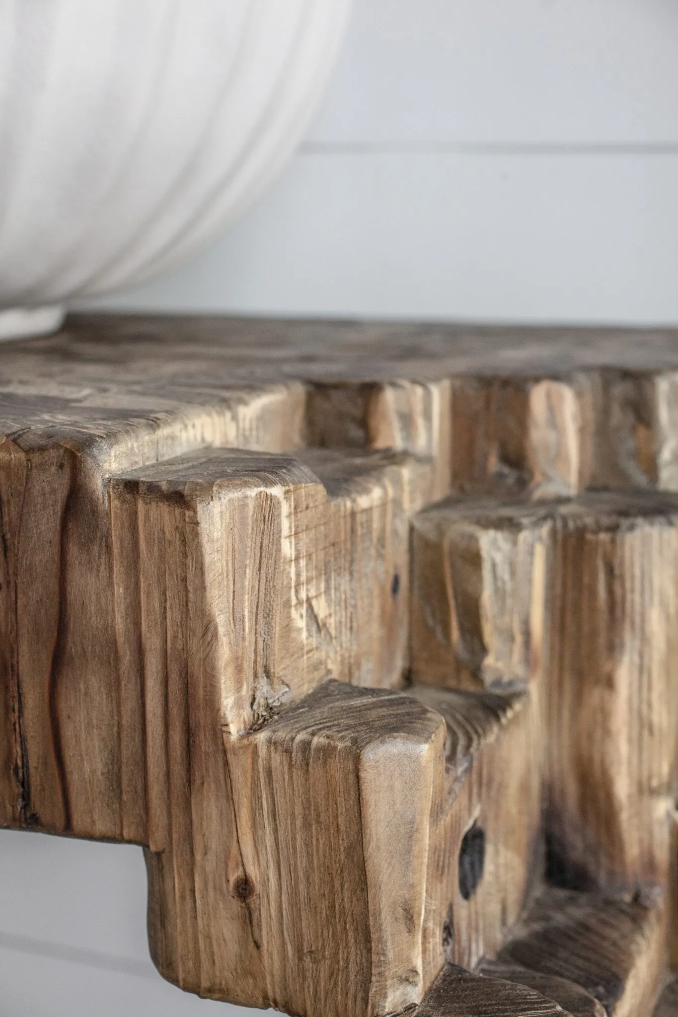 Multifamily interior detail: rough-hewn reclaimed wood console edge below a white ribbed vase
