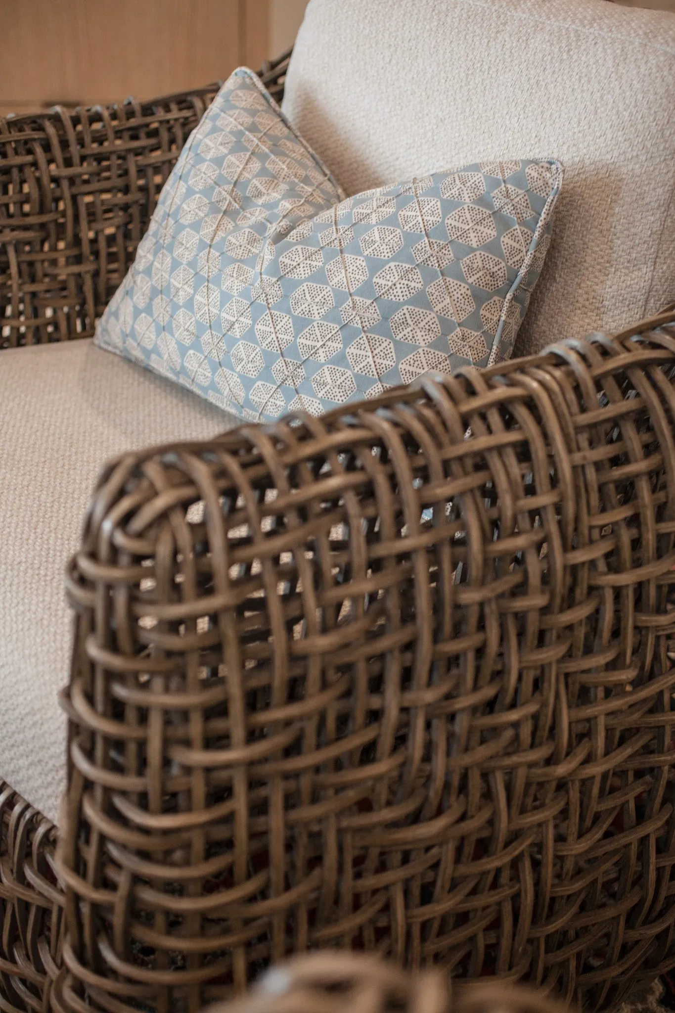 Multifamily interior detail: woven armchair with a cream cushion and blue patterned pillow
