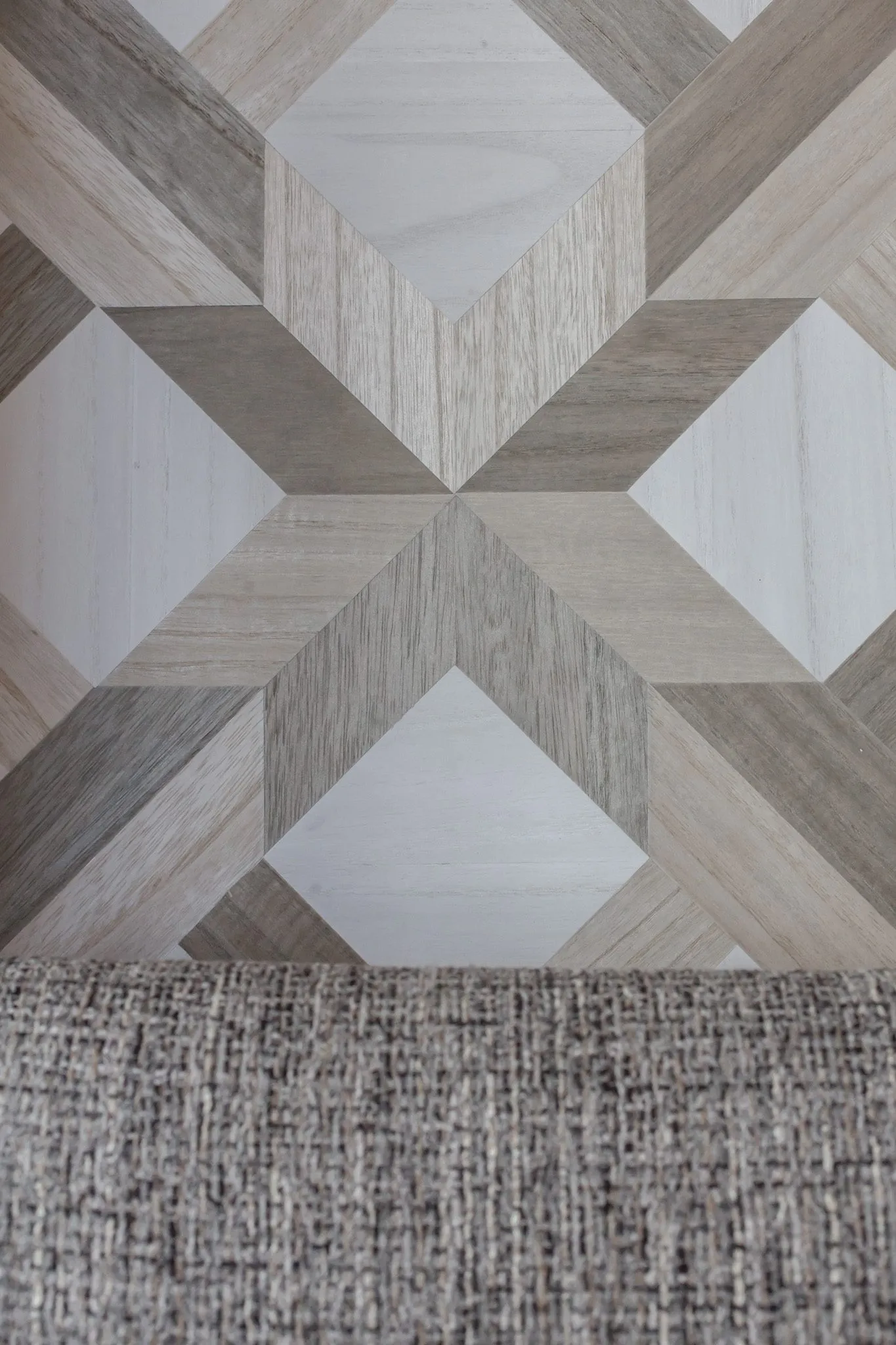 Multifamily interior detail: wood parquet pattern wallcovering above a grey textured banquette back