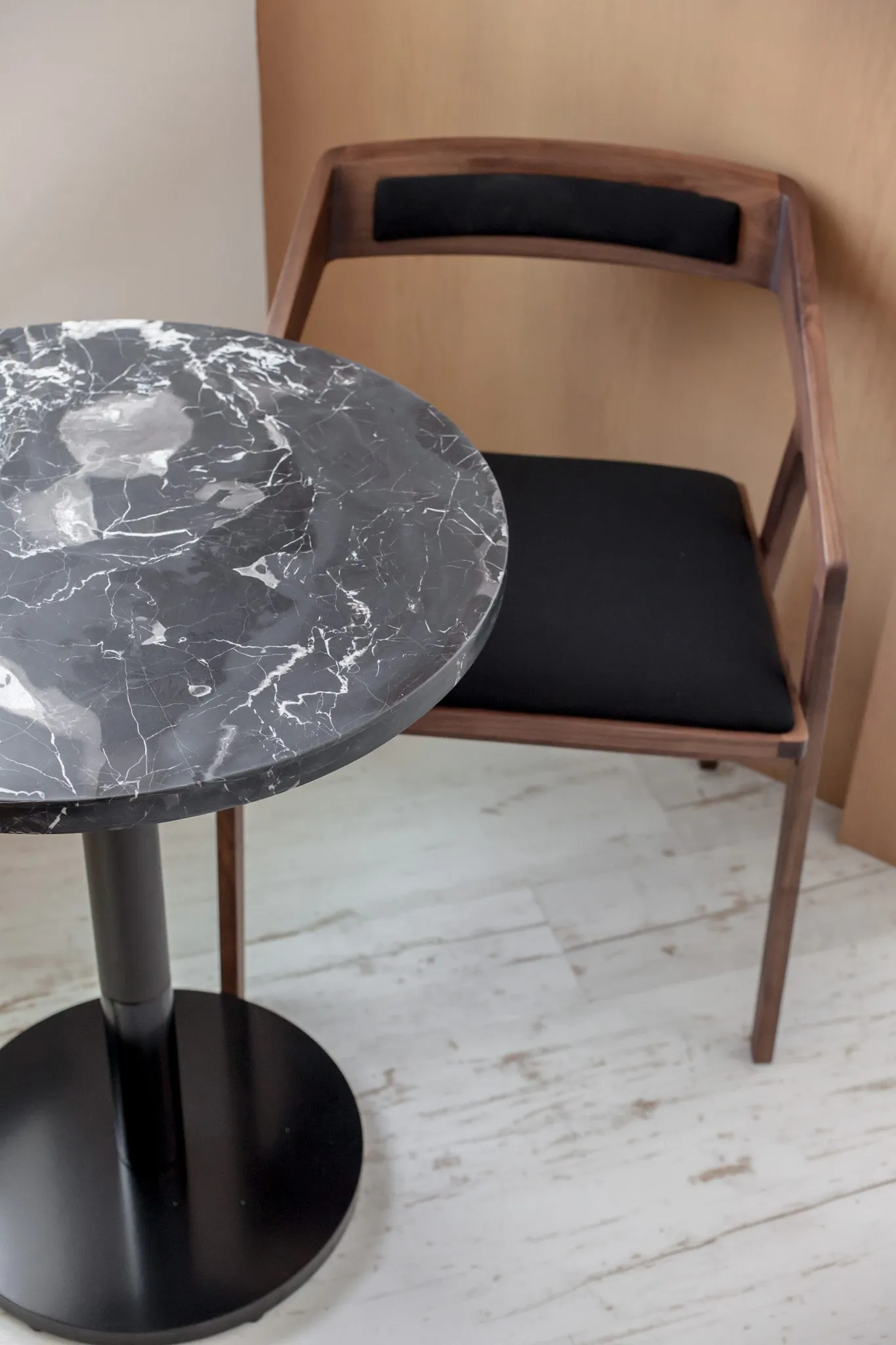 Multifamily interior detail: black marble cafe table with white veining beside a walnut chair with black upholstery