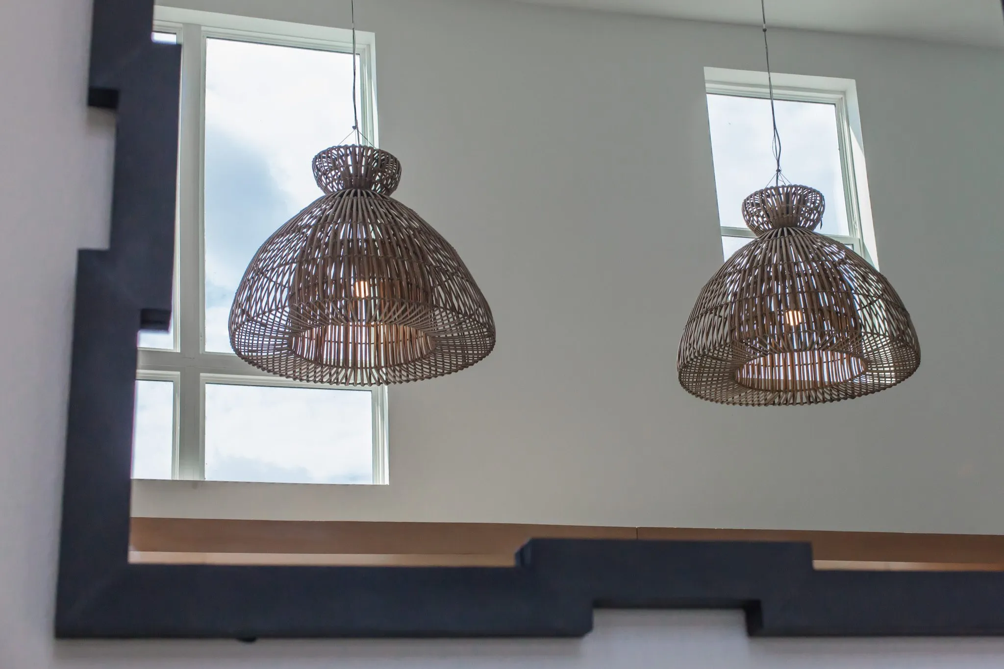 Multifamily interior detail: two woven pendants reflected in a black framed mirror below clerestory windows