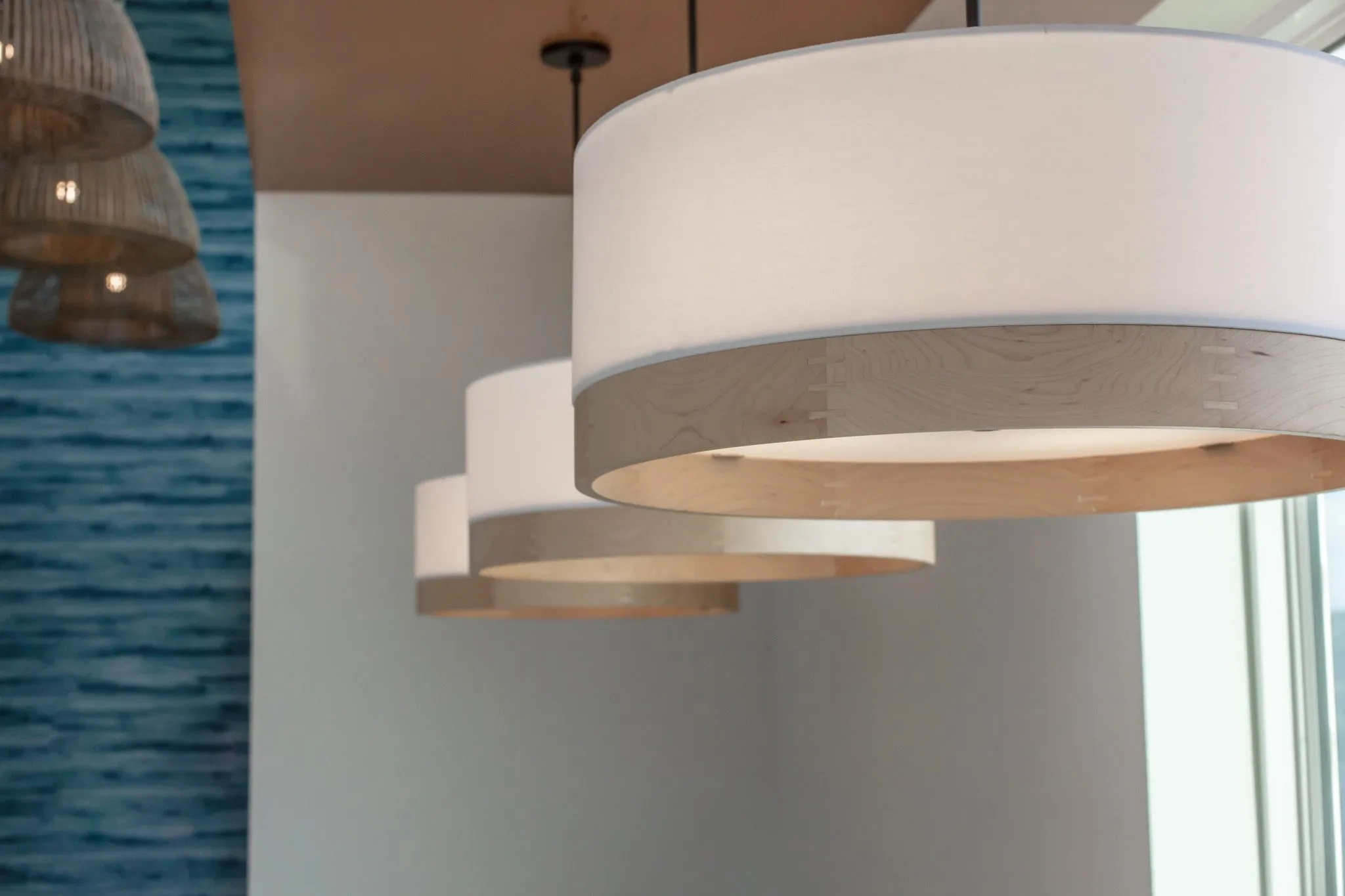 Multifamily interior detail: drum pendants with white shades and wood bands, woven pendants by the blue wall beyond