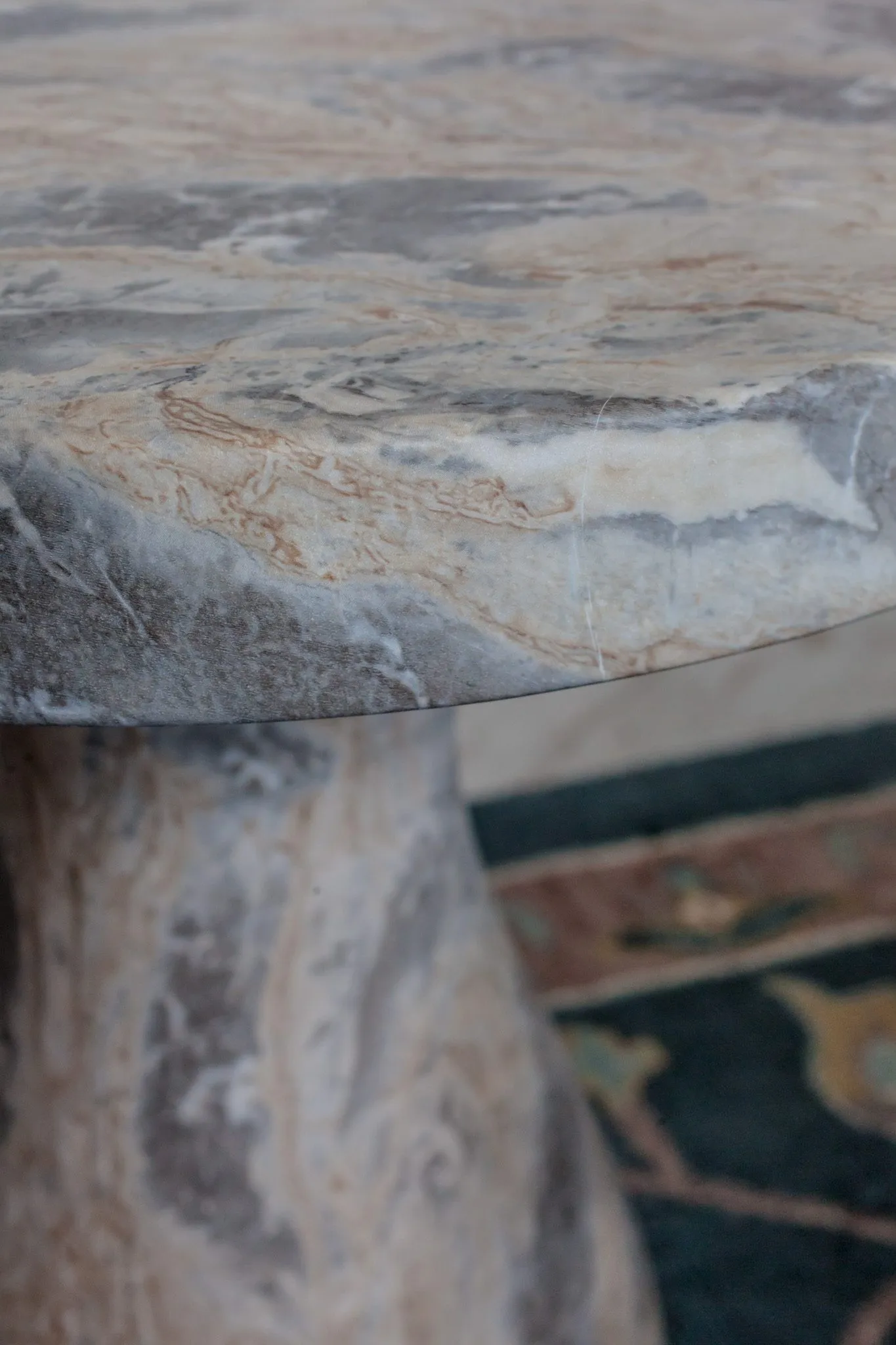 Multifamily interior detail: grey and tan marble side table top and pedestal on a blue rug
