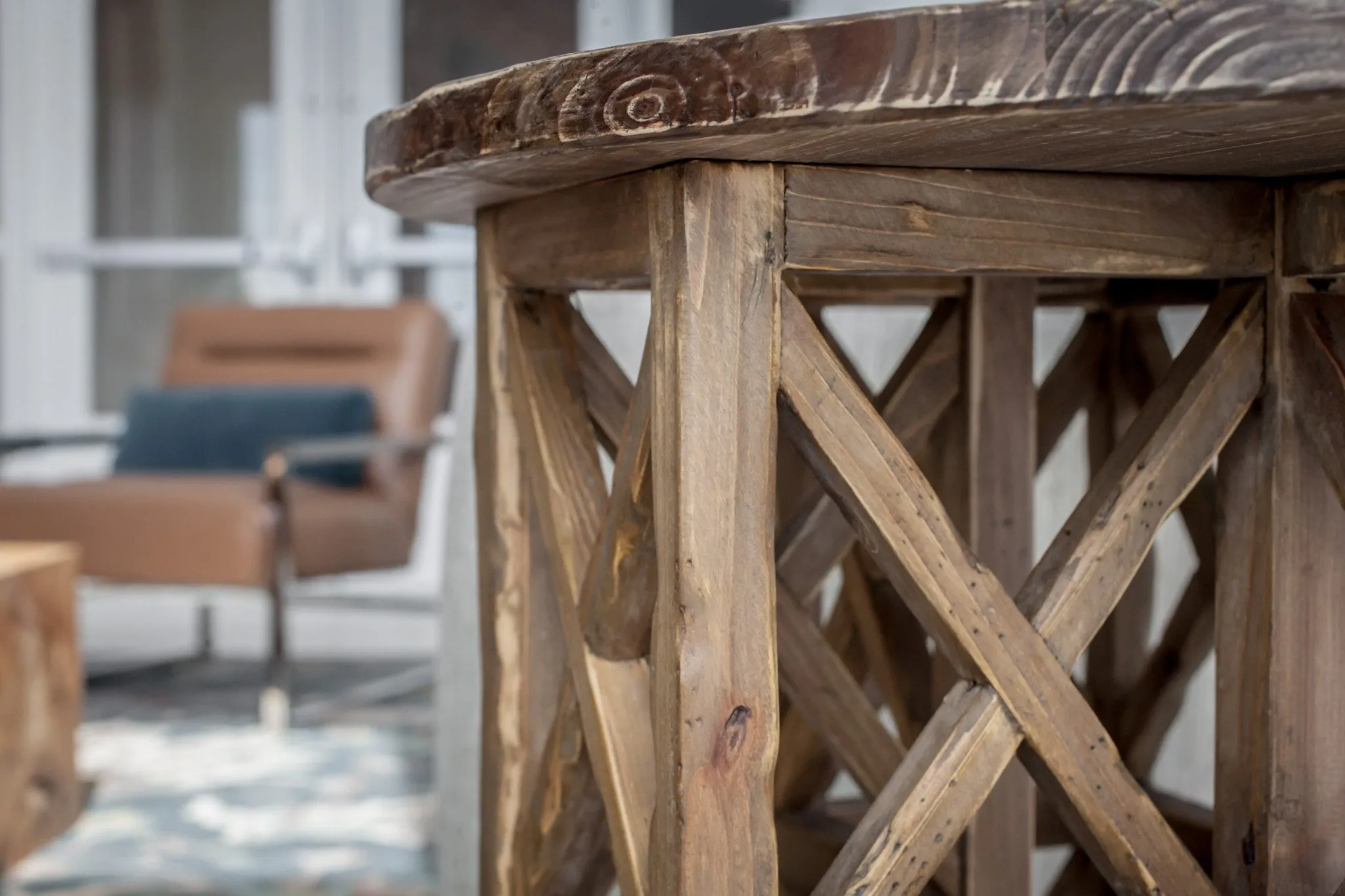 Multifamily interior detail: rustic crossbraced wood side table, a leather chair blurred behind