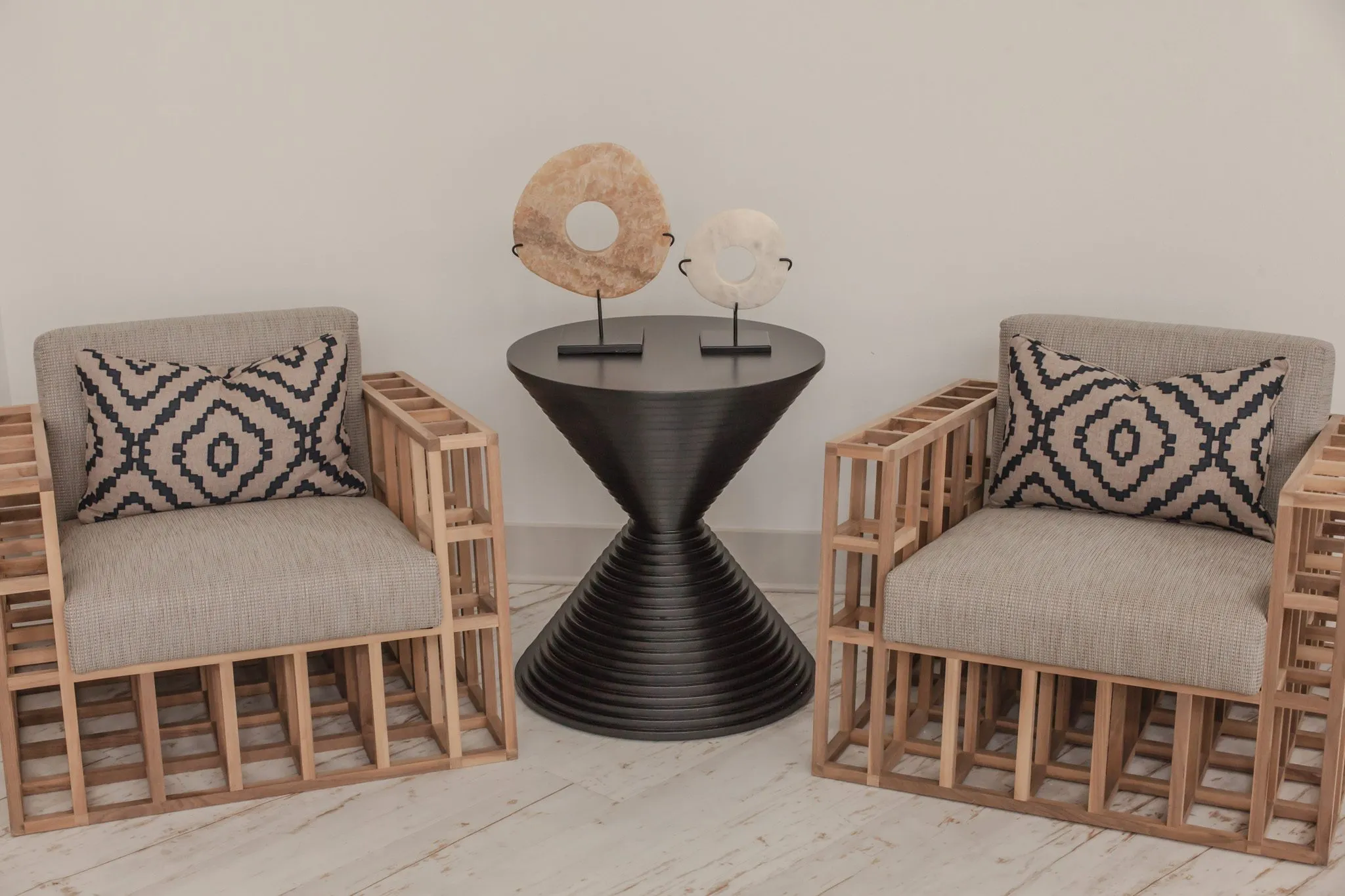 Multifamily interior detail: slatted wood armchairs with patterned pillows flanking a black ribbed hourglass table