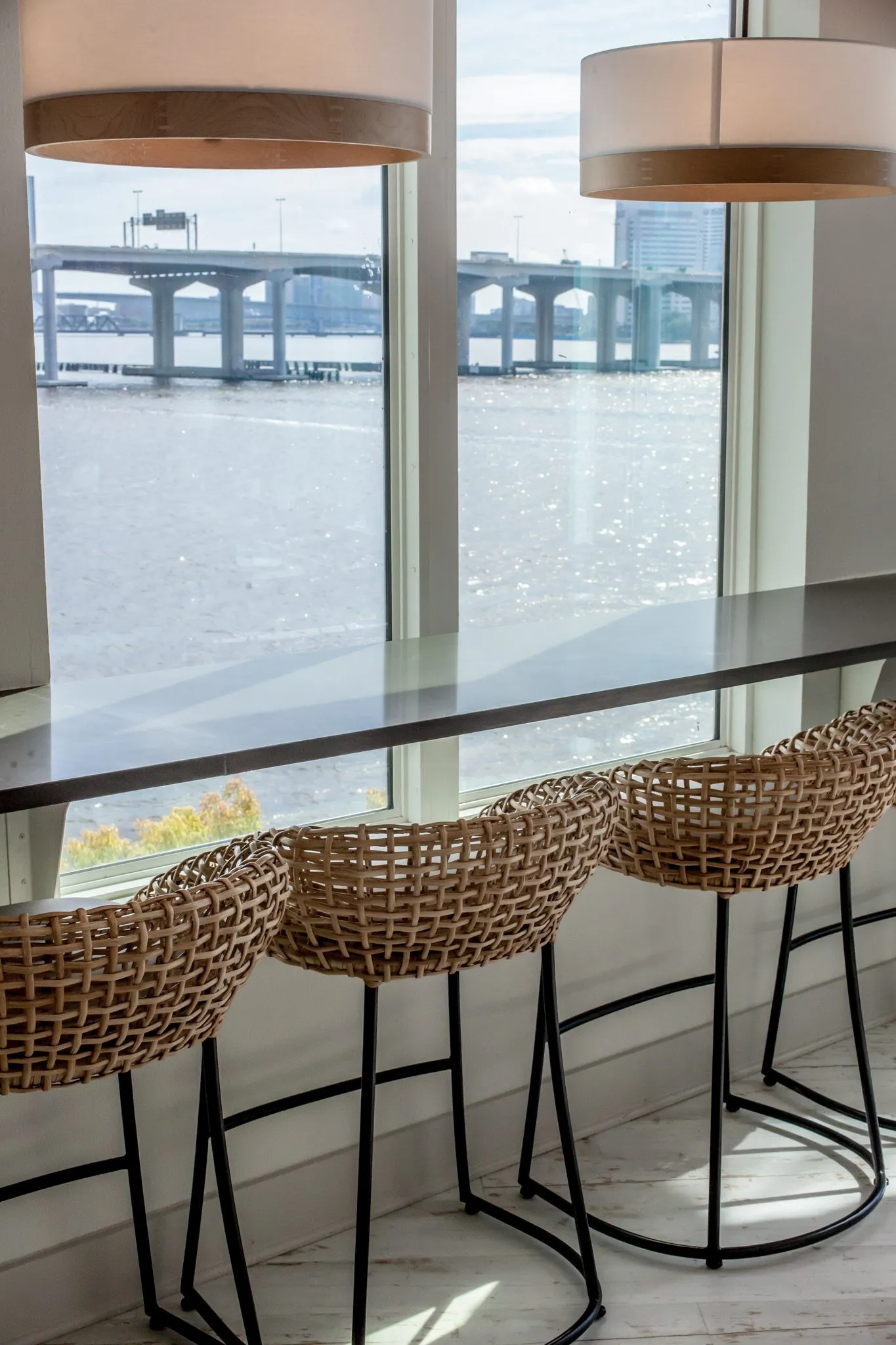 Multifamily amenity window bar with woven stools under drum pendants, the river and bridge through the glass