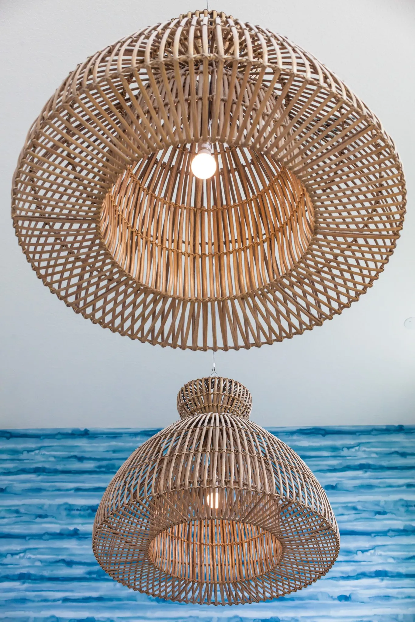 Multifamily interior detail: two woven rattan pendants hung one above the other before the blue water pattern wall
