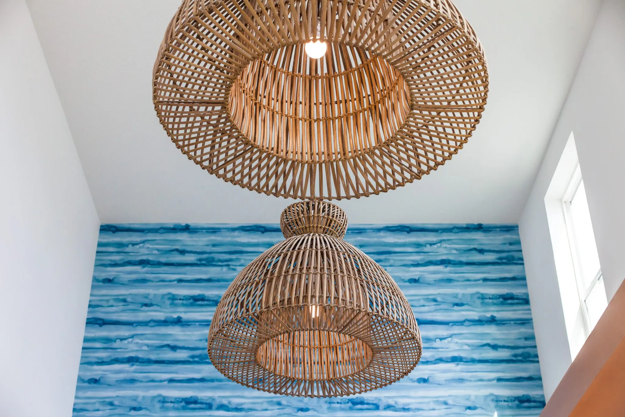 Multifamily interior detail: looking up at stacked rattan pendants against the blue water pattern wall