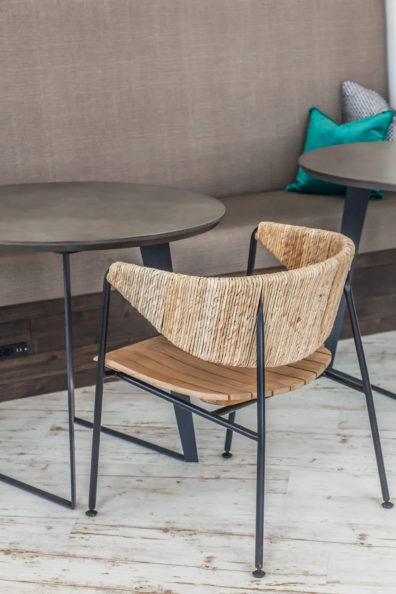 Multifamily interior detail: woven back chair with a slatted wood seat at a round table before the grey banquette