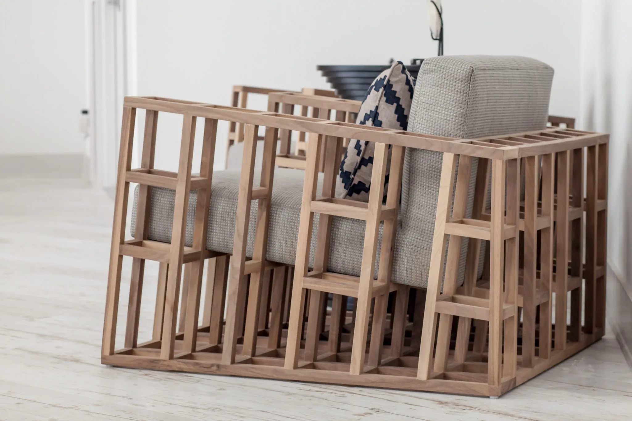 Multifamily interior detail: side view of a slatted wood cube armchair with a grey cushion and patterned pillow