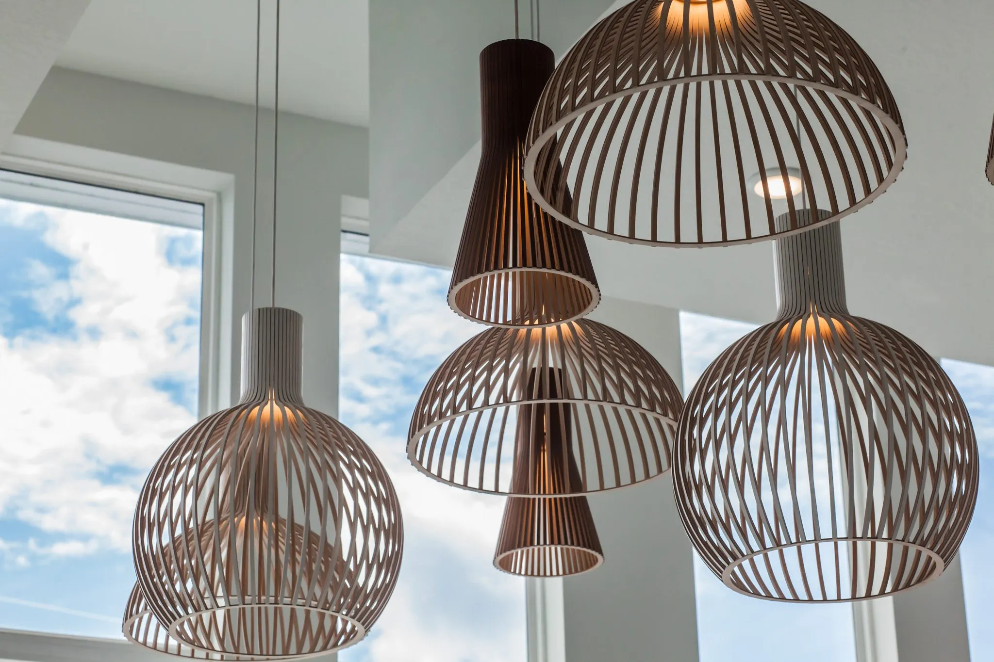 Multifamily interior detail: walnut and pale wood ribbon pendants against tall windows and sky