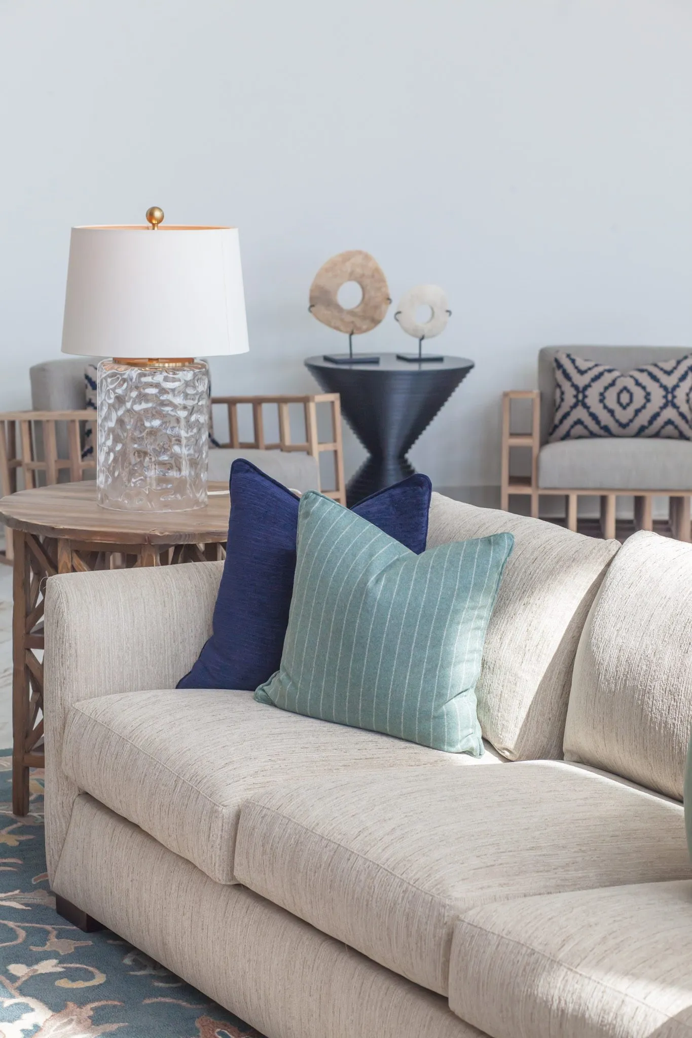 Multifamily interior detail: cream sofa with navy and green pillows, a glass lamp and slatted armchairs beyond