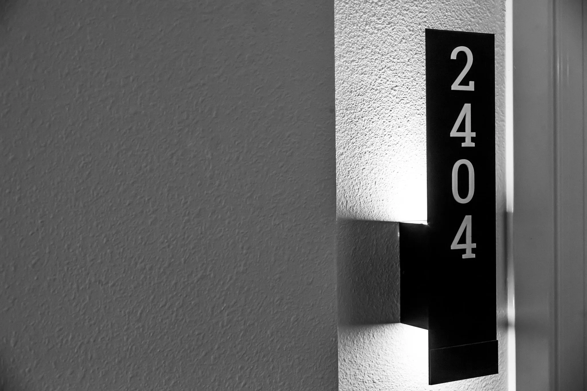 Multifamily interior detail: illuminated apartment number sign on textured plaster, in black and white