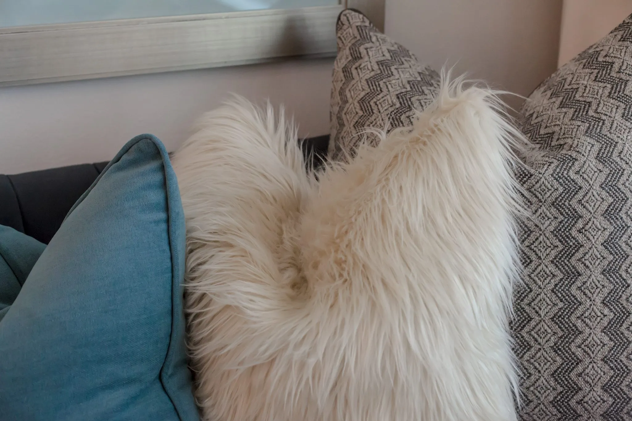 Multifamily interior detail: sheepskin pillow between teal and grey zigzag pillows on a sofa
