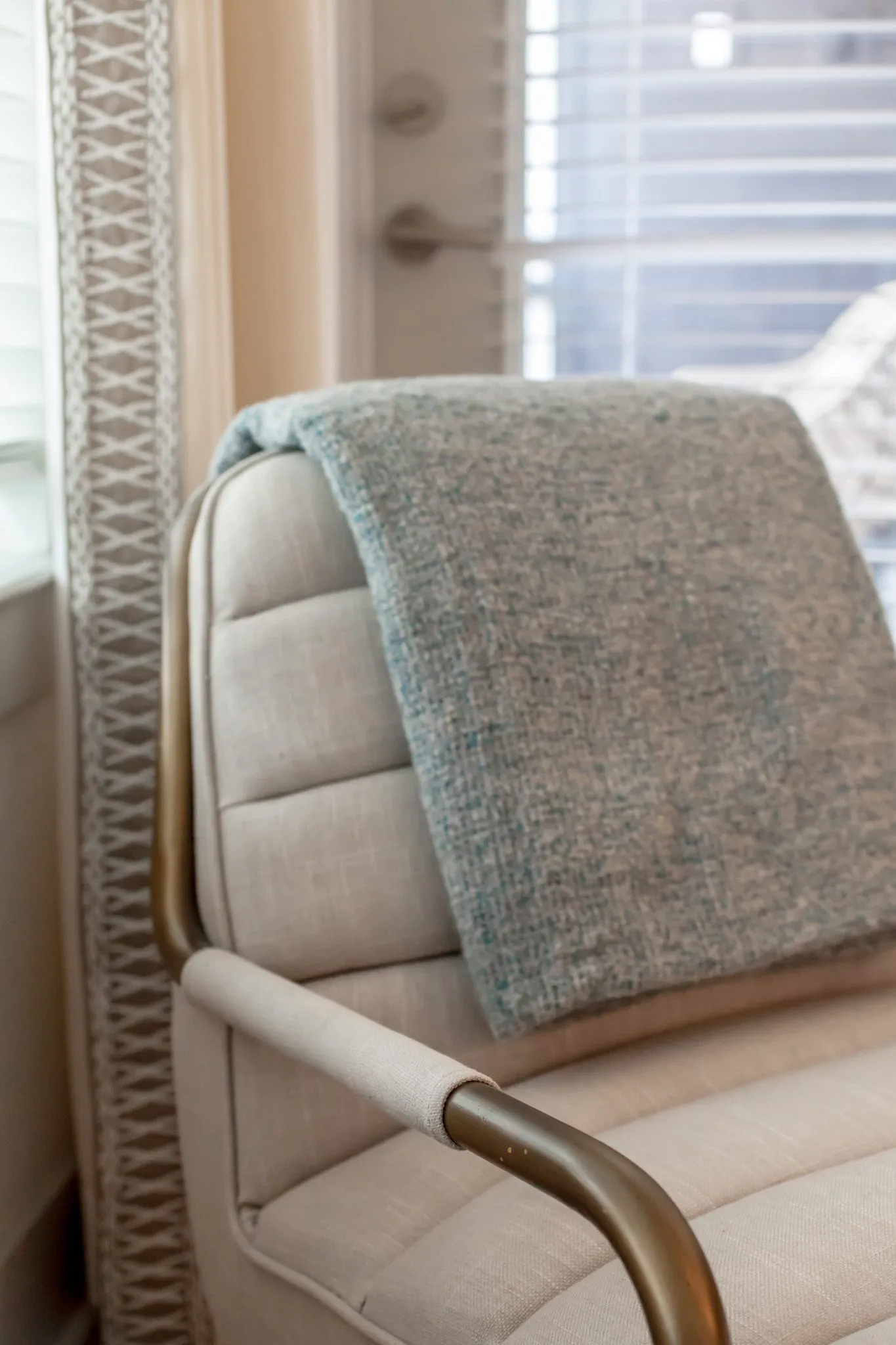 Multifamily interior detail: grey throw draped over a cream channel tufted armchair with a brass frame