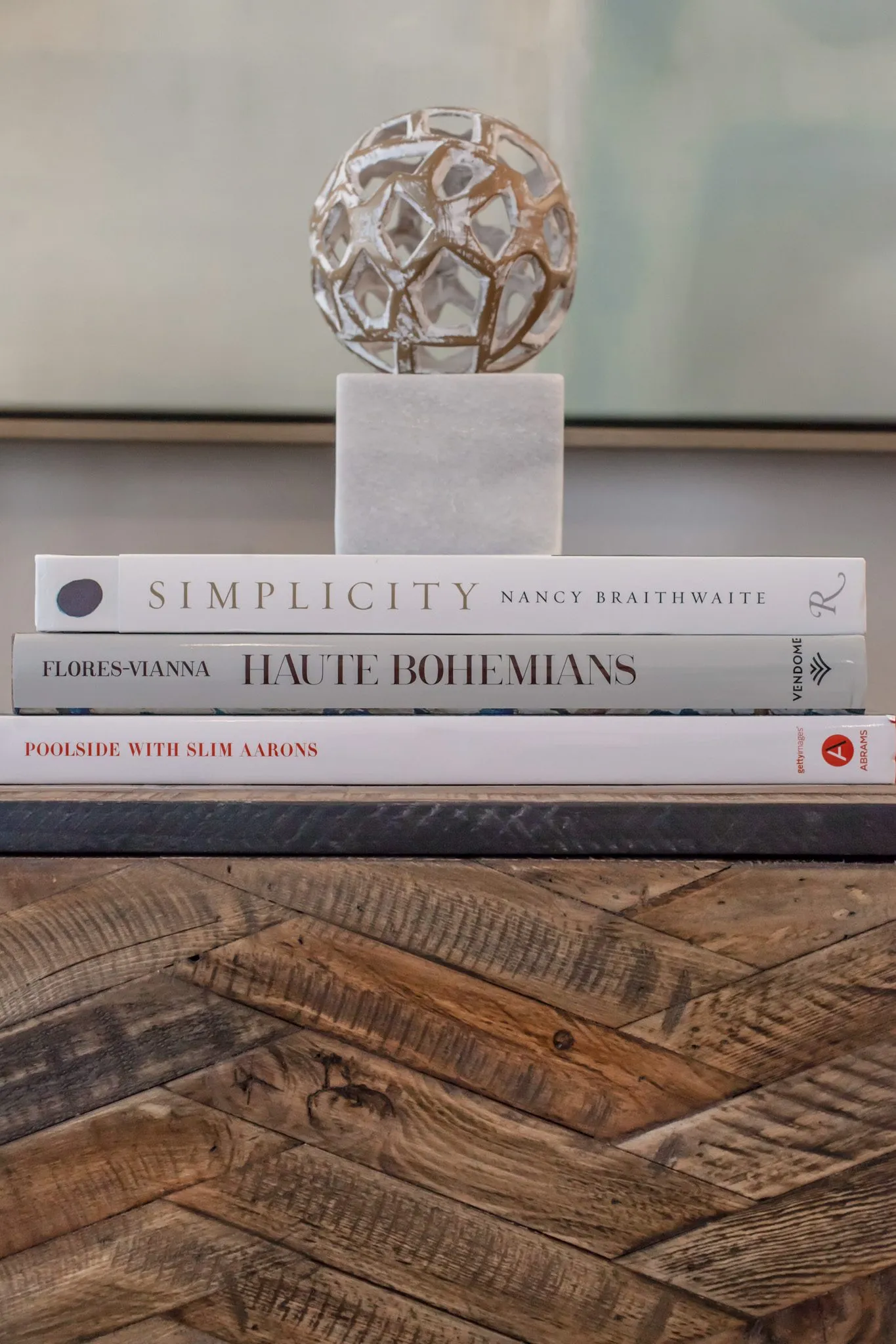 Multifamily interior detail: faceted metal orb on a marble block atop stacked books on a herringbone wood sideboard