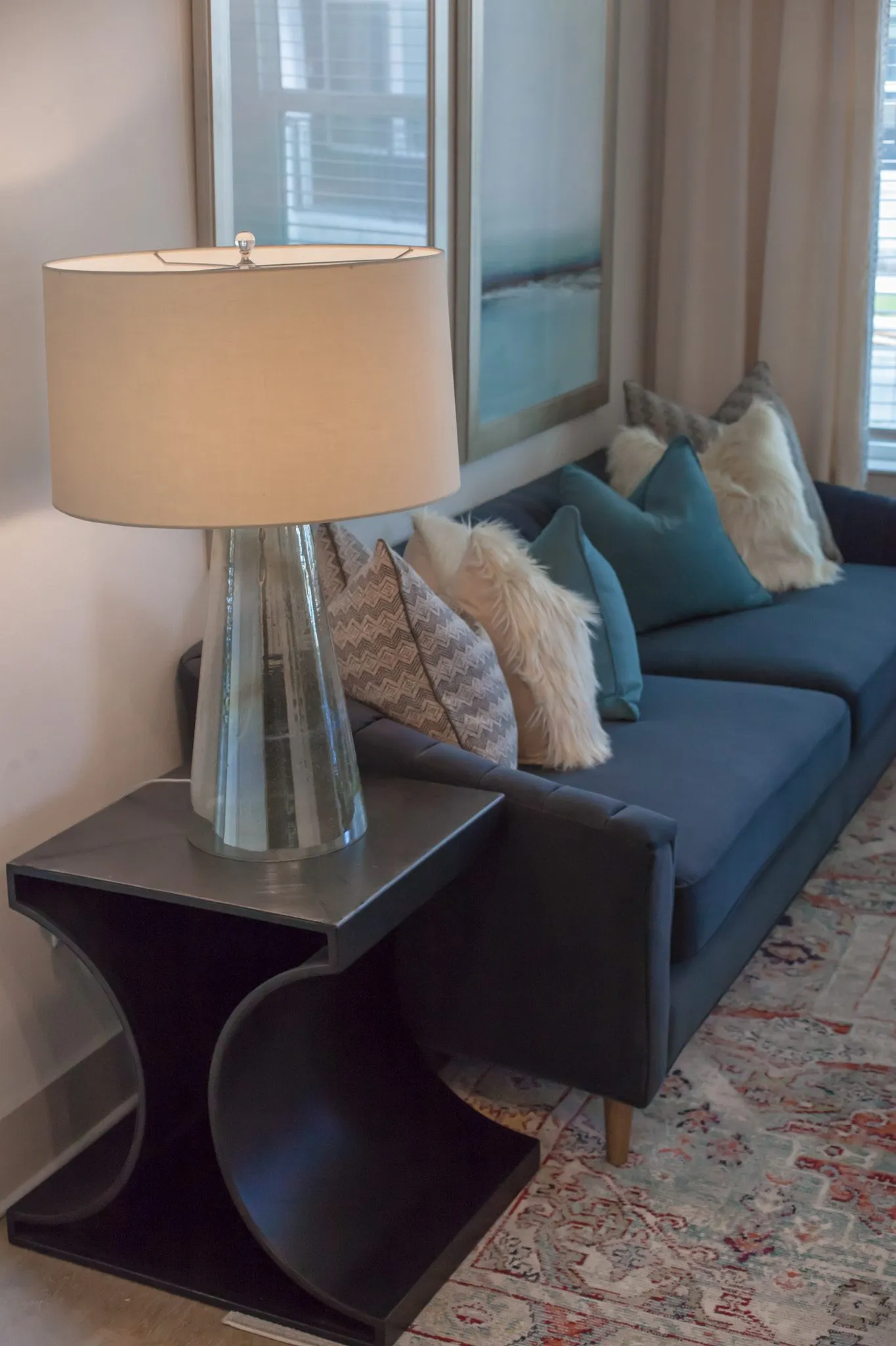 Multifamily interior detail: glass lamp on a black curved side table beside a navy sofa with teal and sheepskin pillows